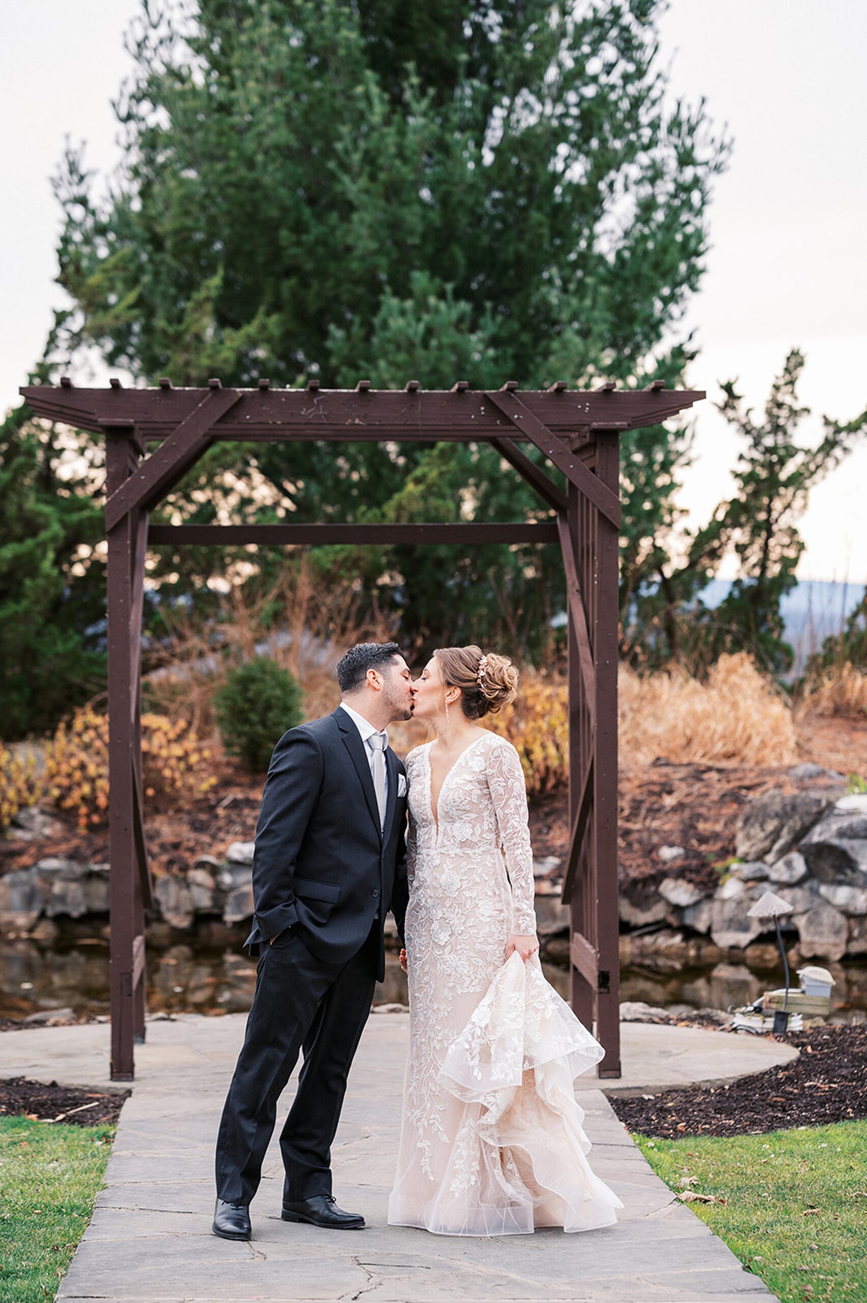 Newlyweds kiss and hold hands while standing under a wooden gazebo at a Crystal Springs Wedding