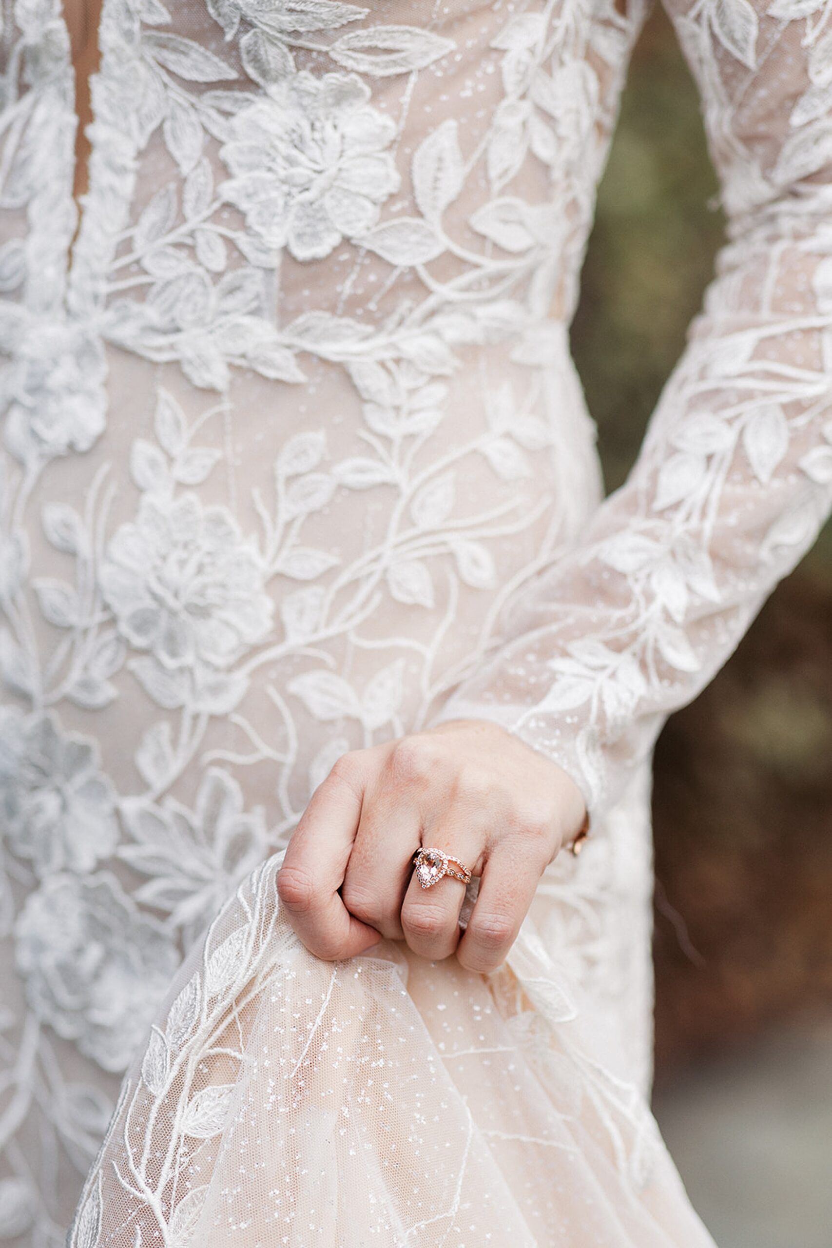 Details of a bride in a white lace dress holding her train while walking