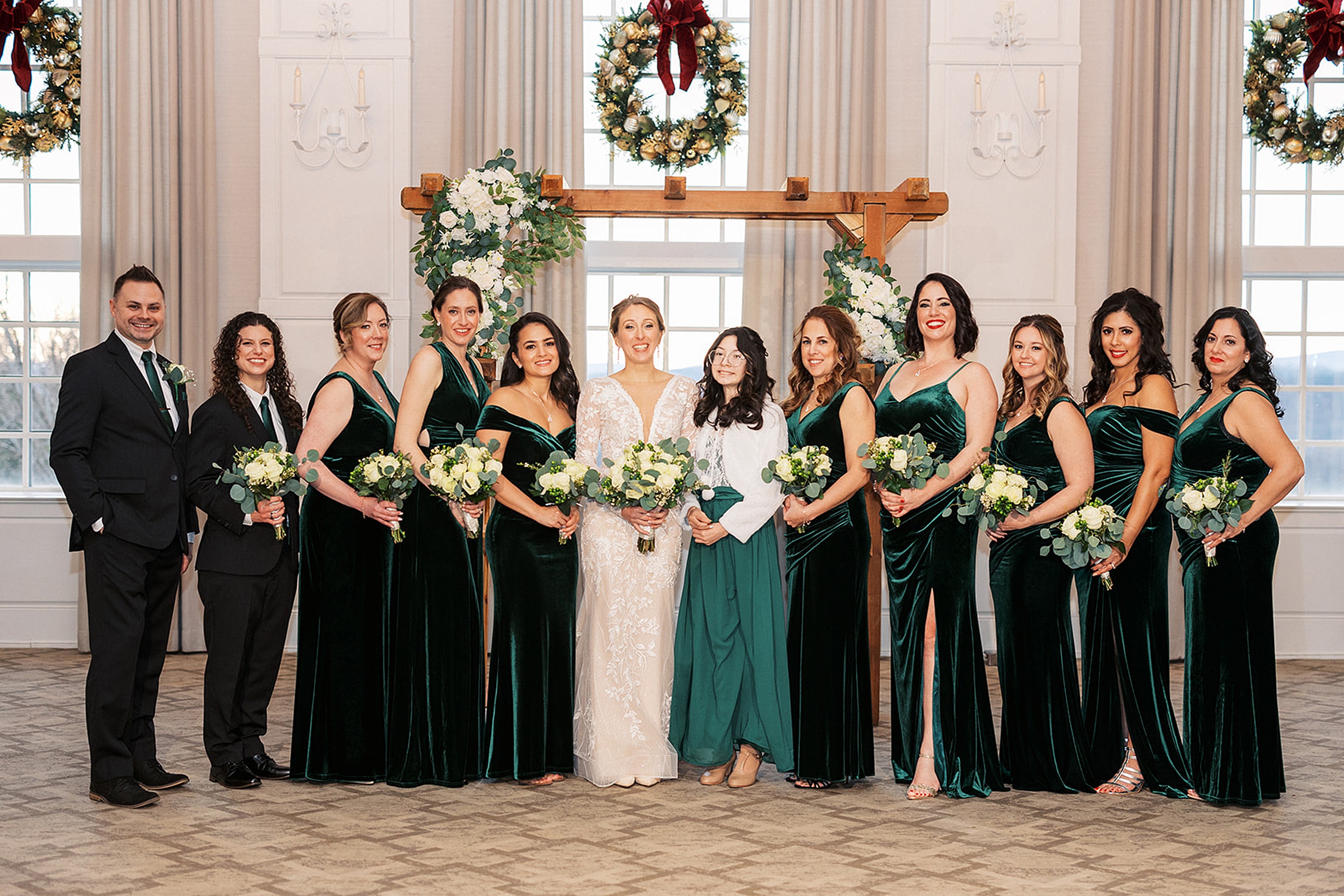 A bride stands under a wooden arbor holding her bouquet with her large bridal party all in green at a Crystal Springs Wedding