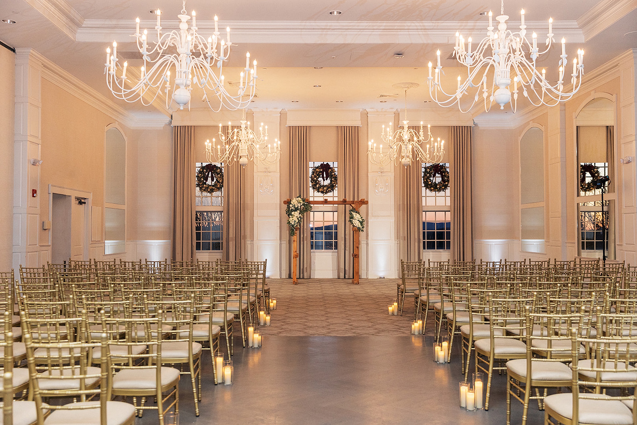 Details of a wedding ceremony setup indoors with gold chairs, candles and chandeliers
