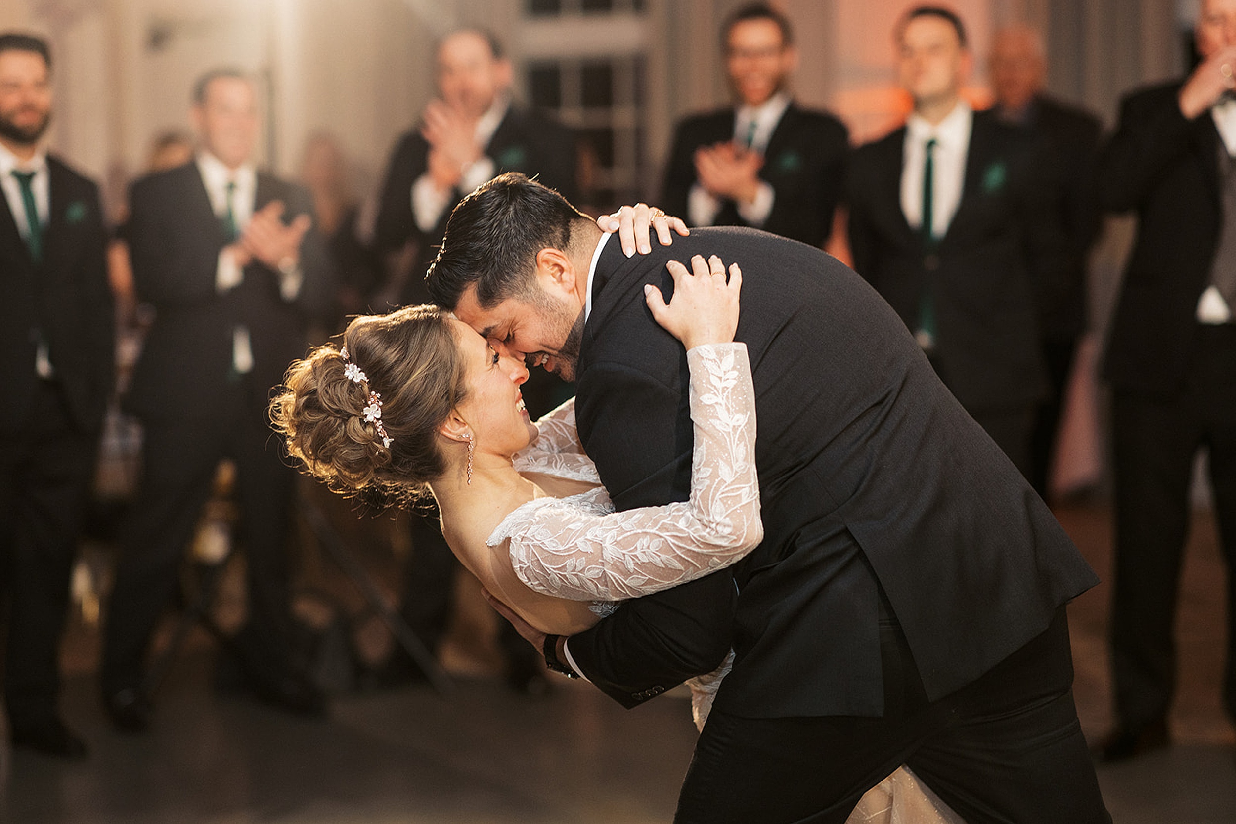 Newlyweds dance and dip during their first dance with the groomsmen cheering behind them at a Crystal Springs Wedding