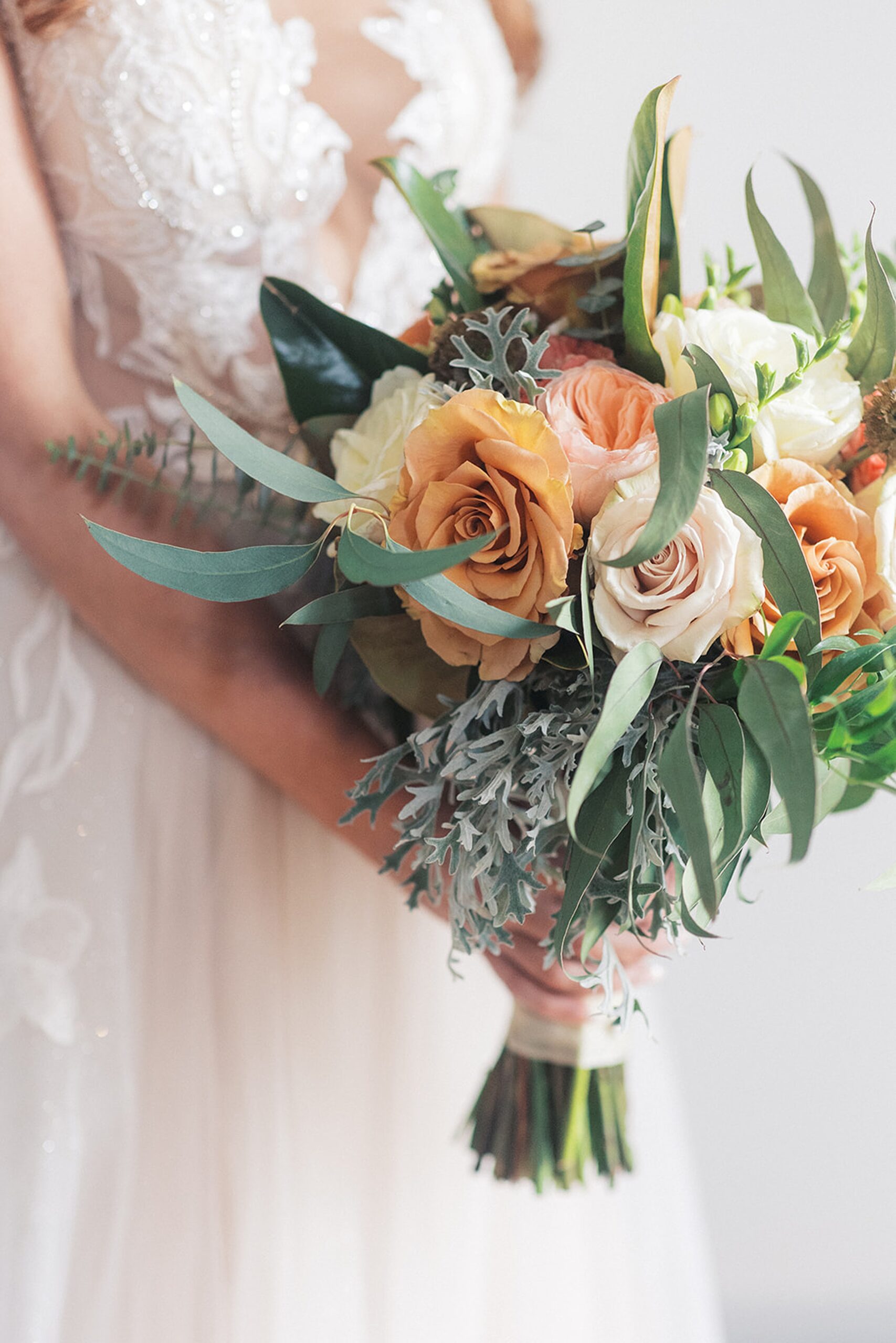 Details of a bride in a white lace dress holding her orange and white bouquet