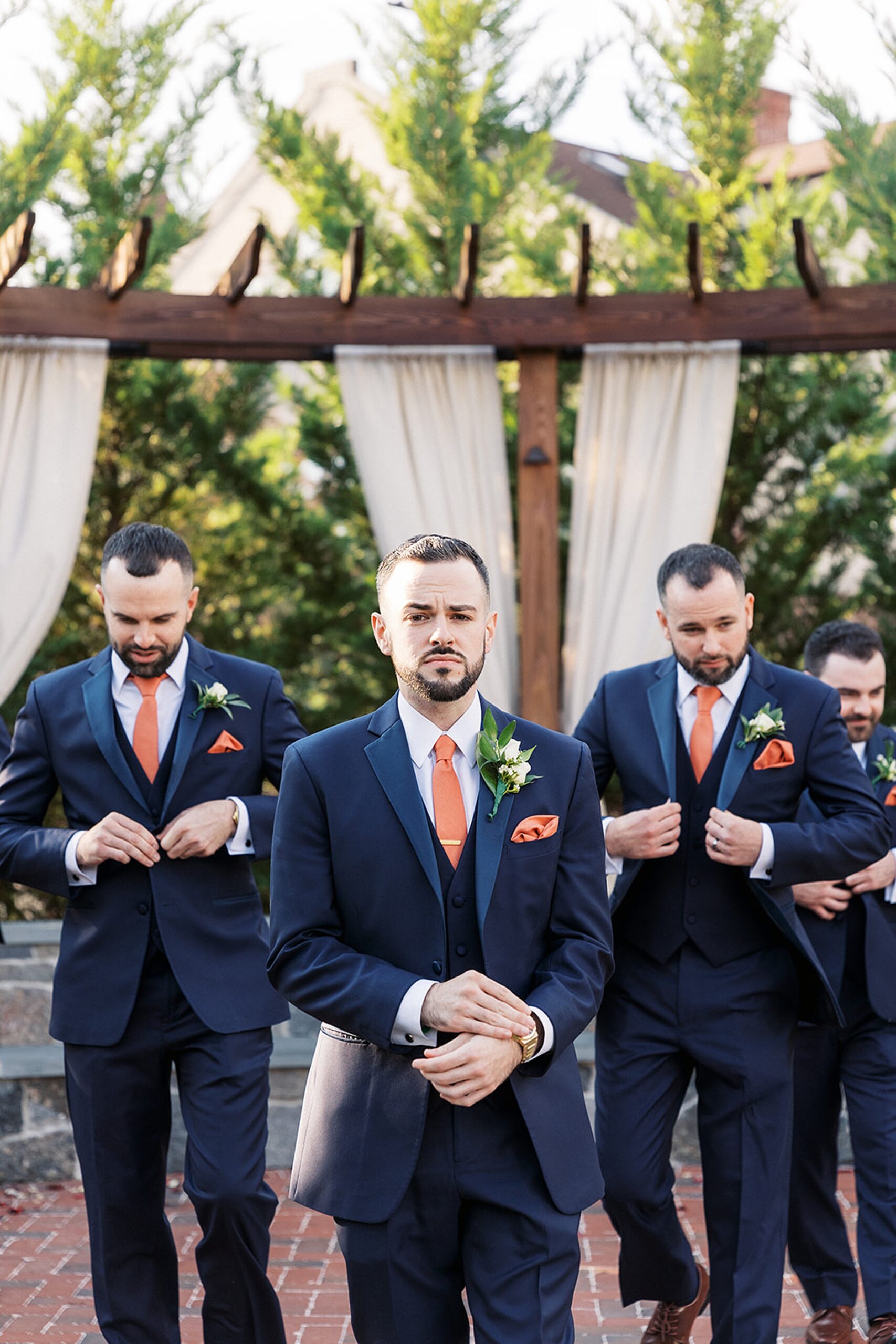 Groomsmen walk through a brick path in a garden adjusting their suits at a David's country inn wedding