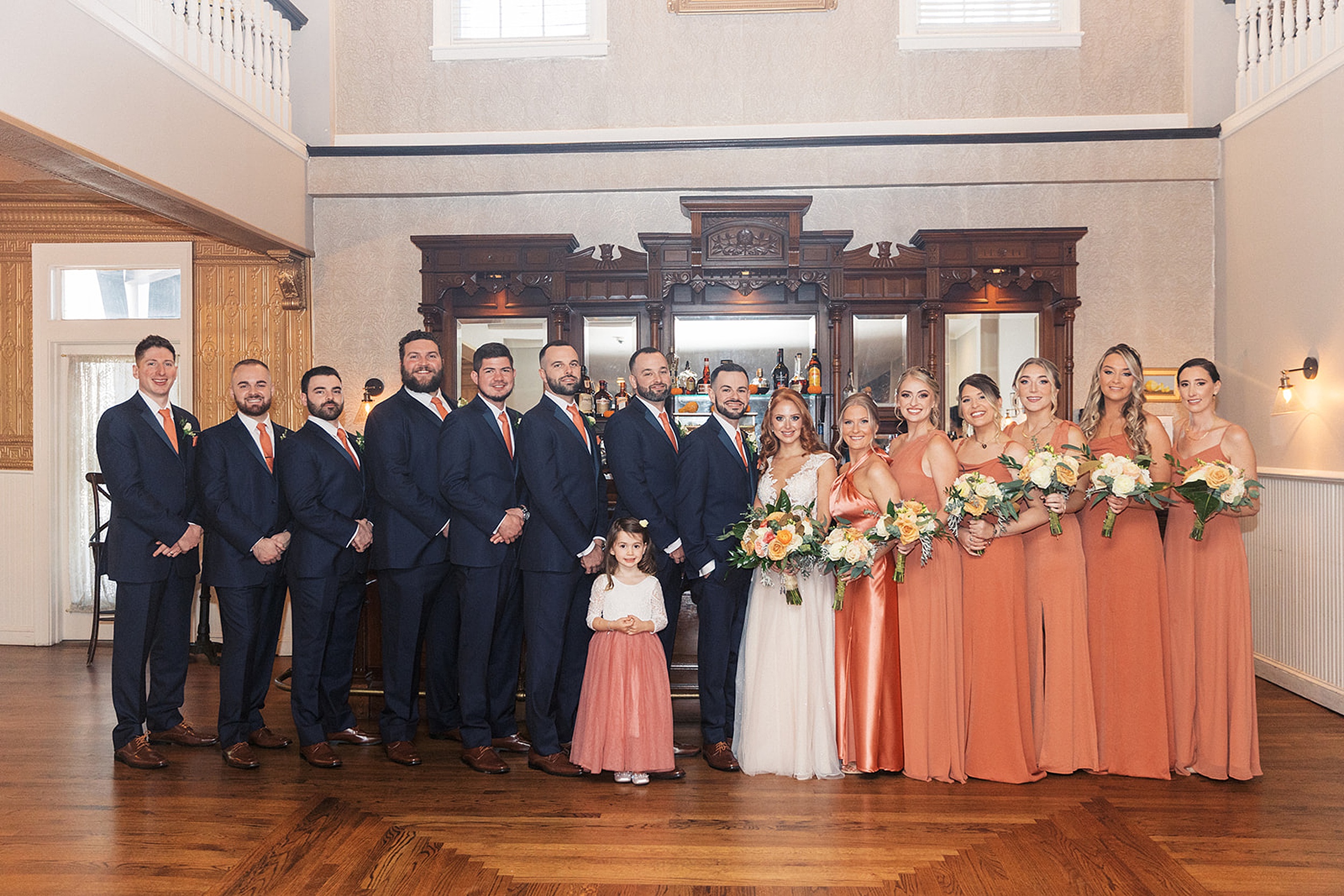 Newlyweds stand with their wedding parties in front of an antique bar