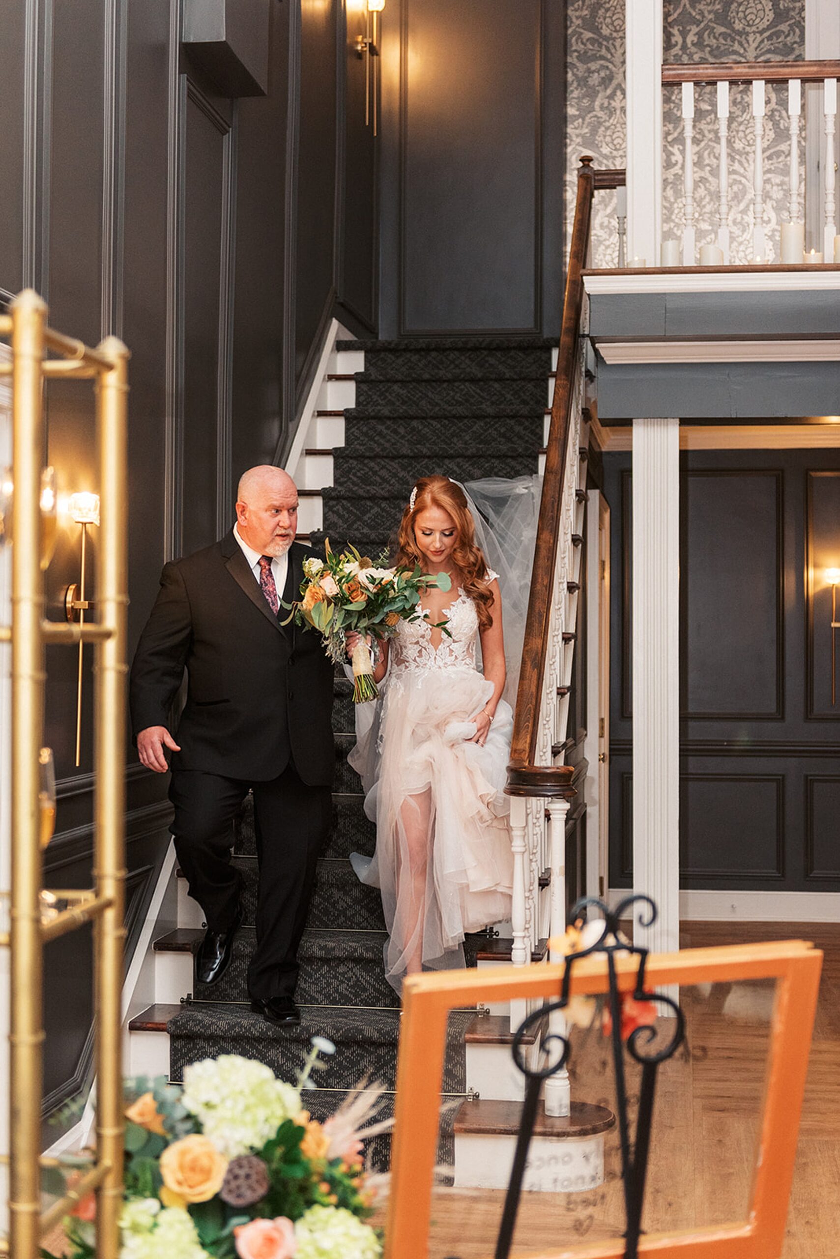 A father walks his daughter in to her wedding ceremony down a flight of stairs in a white lace dress at a David's country inn wedding