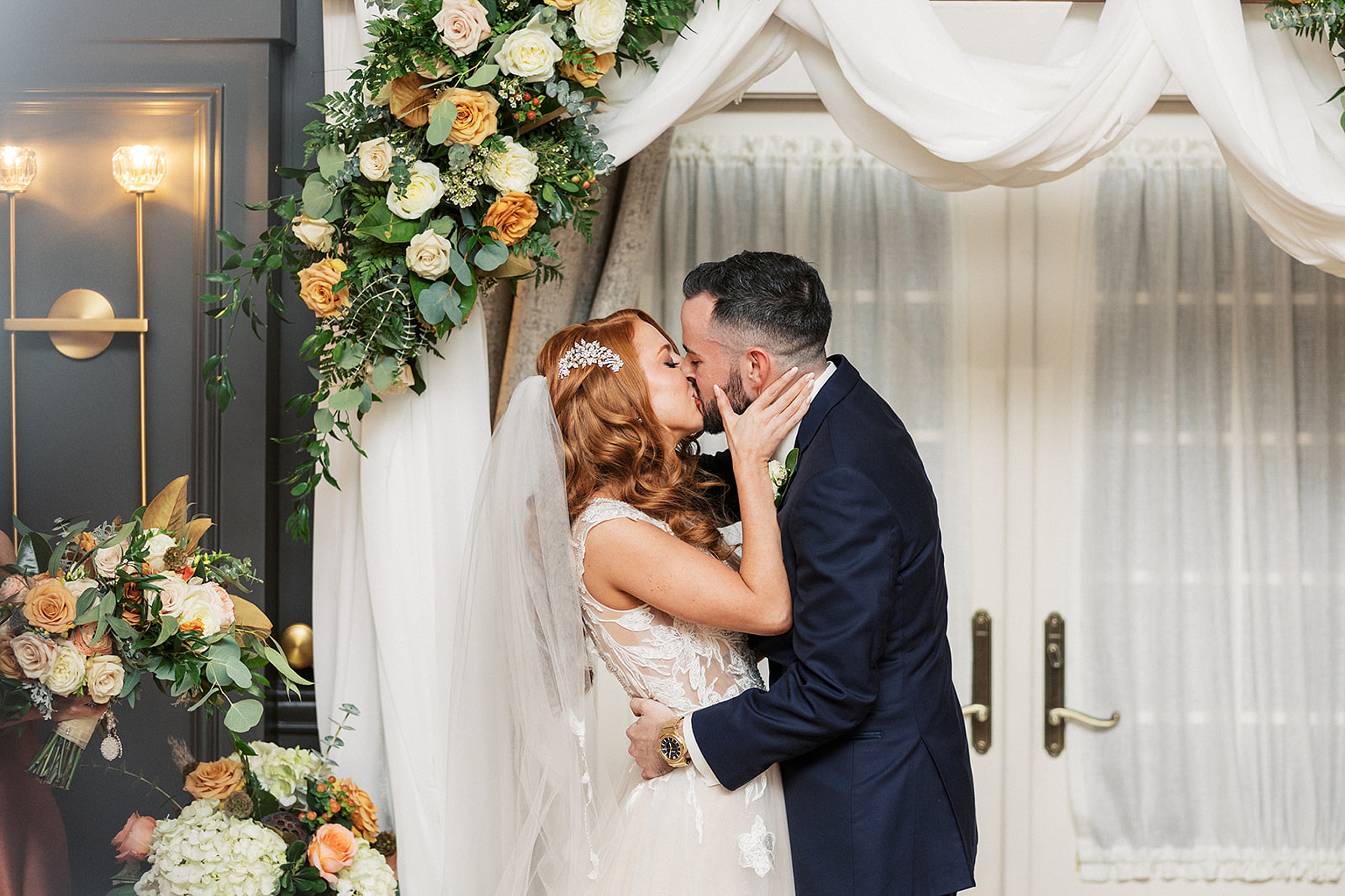 Newlyweds kiss under the arbor covered in white linen and flowers at a David's country inn wedding