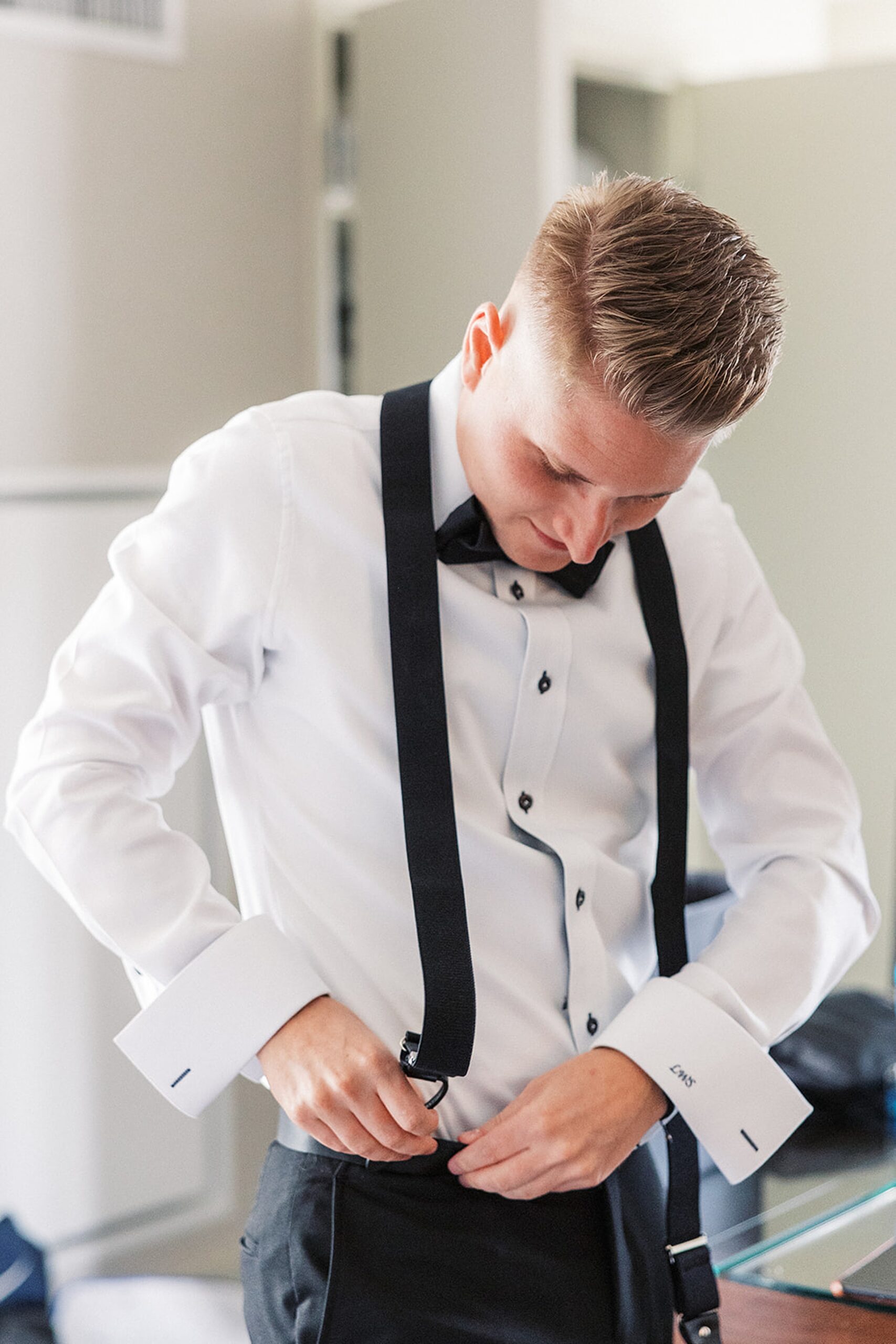 A groom attaches his suspenders while getting ready for his wedding