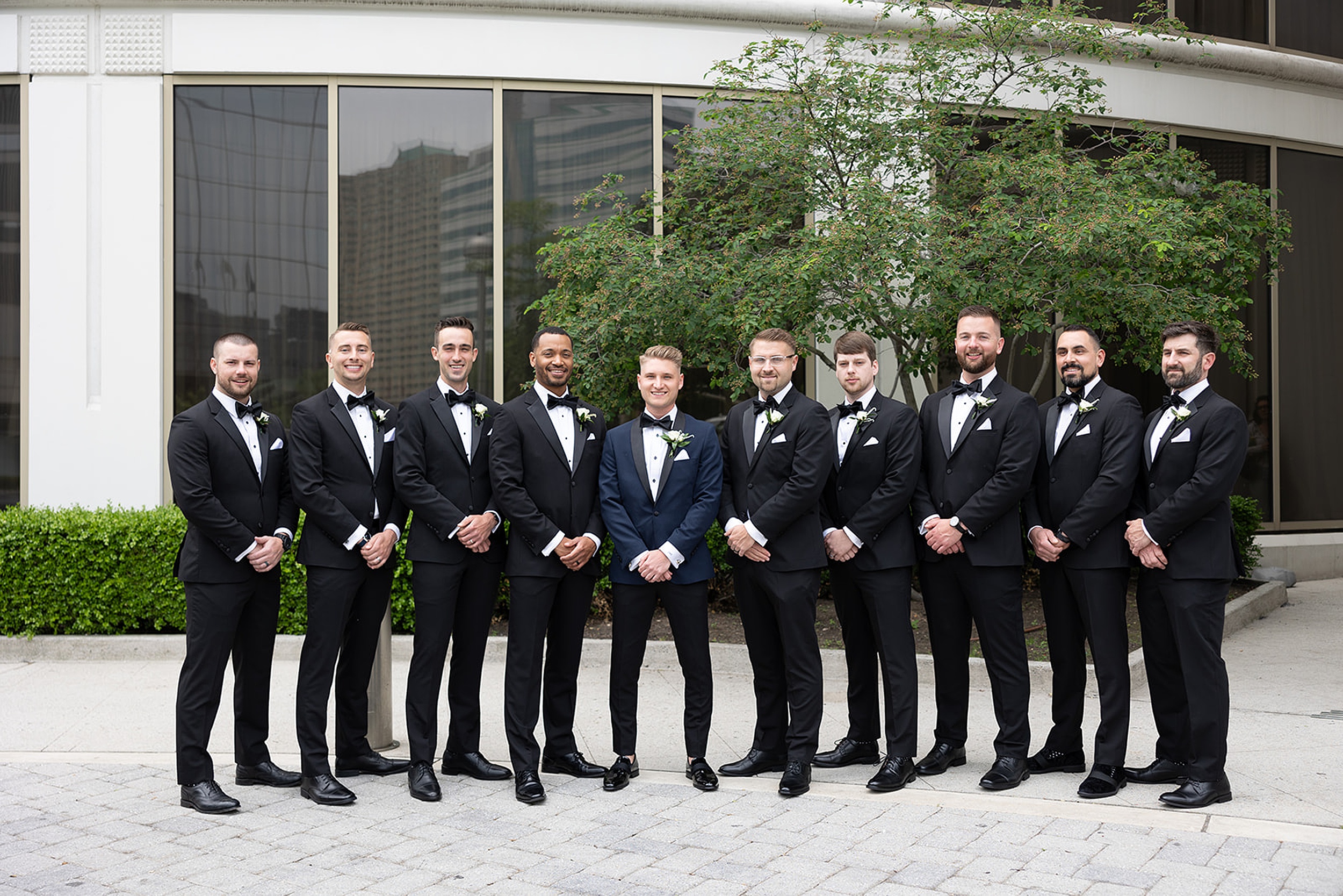 A groom in a blue tuxedo stands with his groomsmen all wearing black
