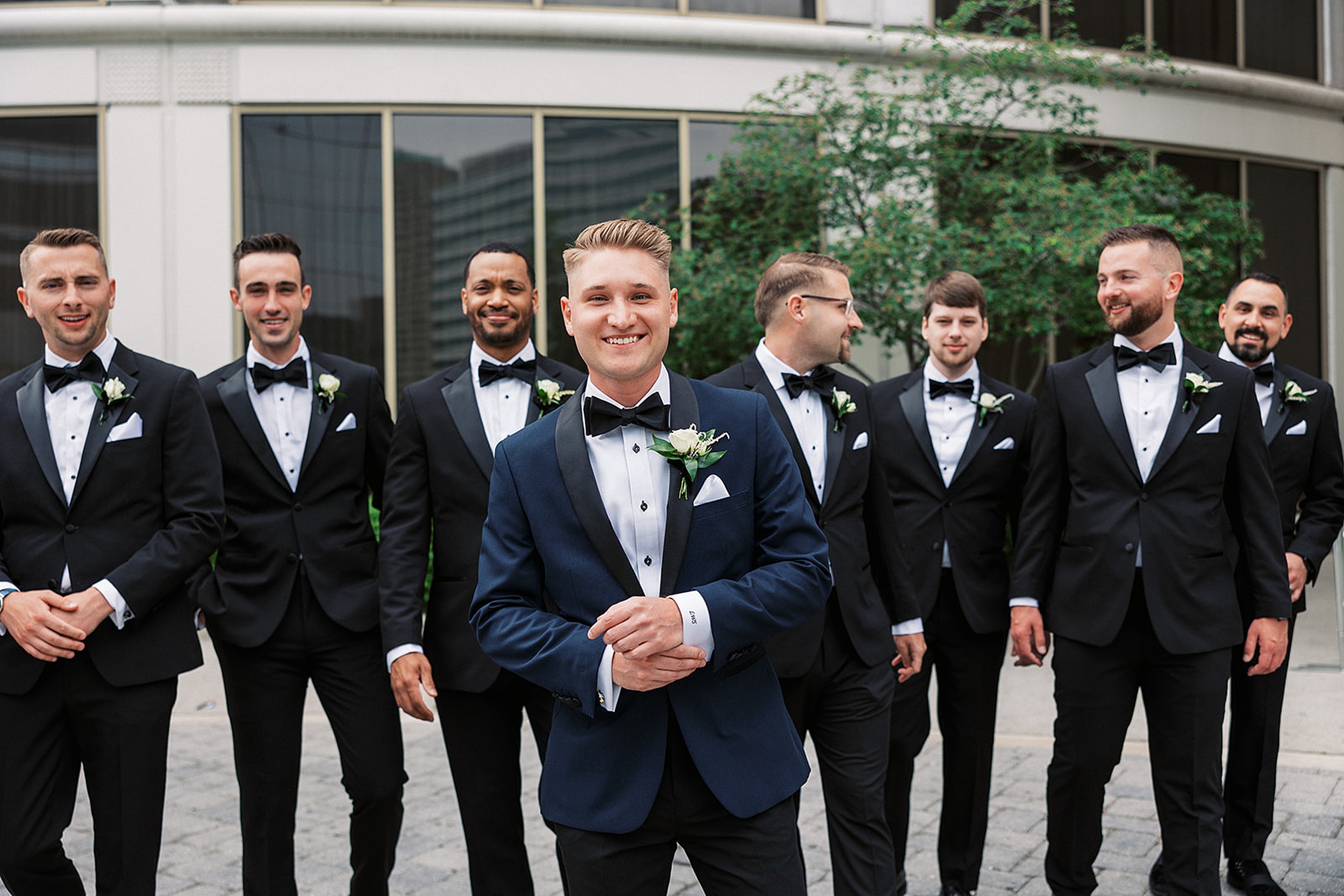 A groom adjusts his cuffs while standing on a patio with his groomsmen at a Hudson House wedding