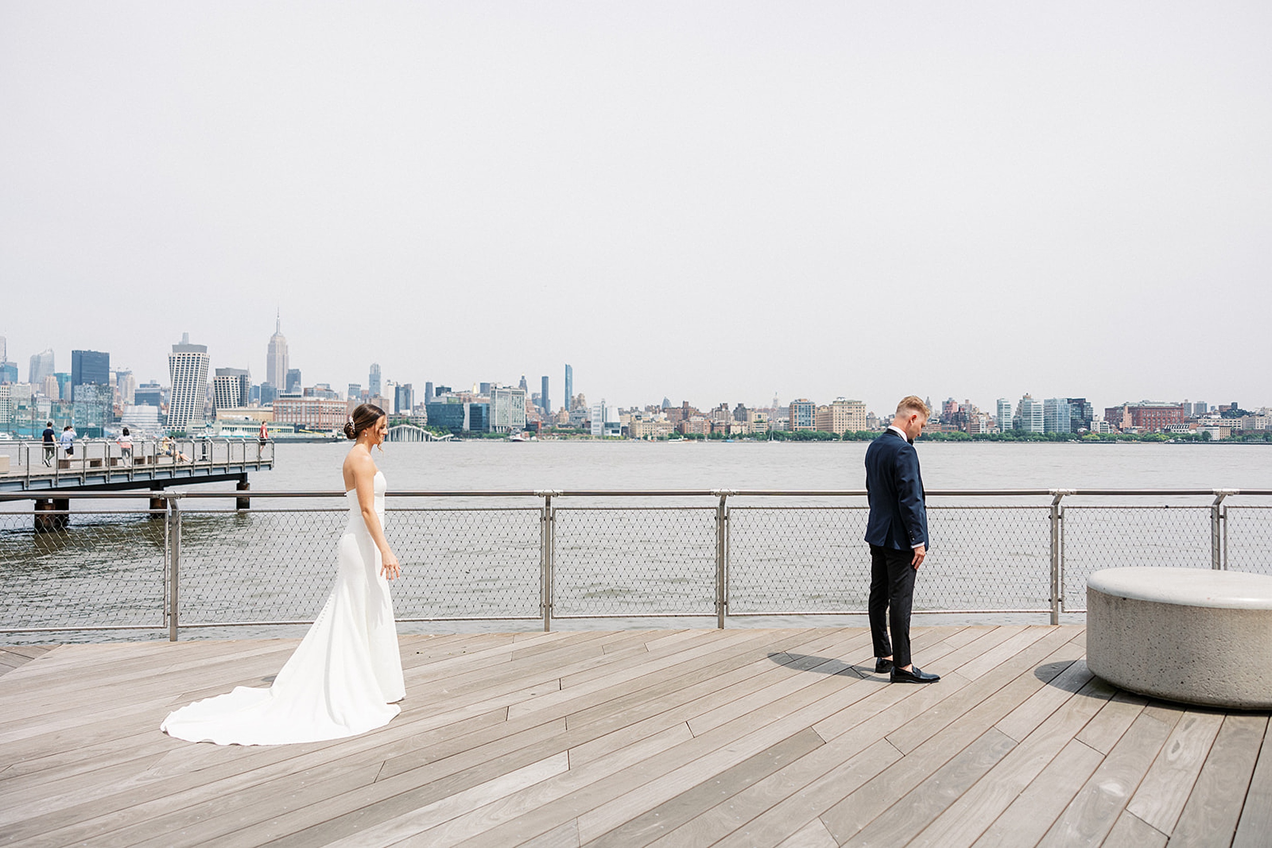 A groom waits for his bride to call him for their first look on a waterfront boardwalk