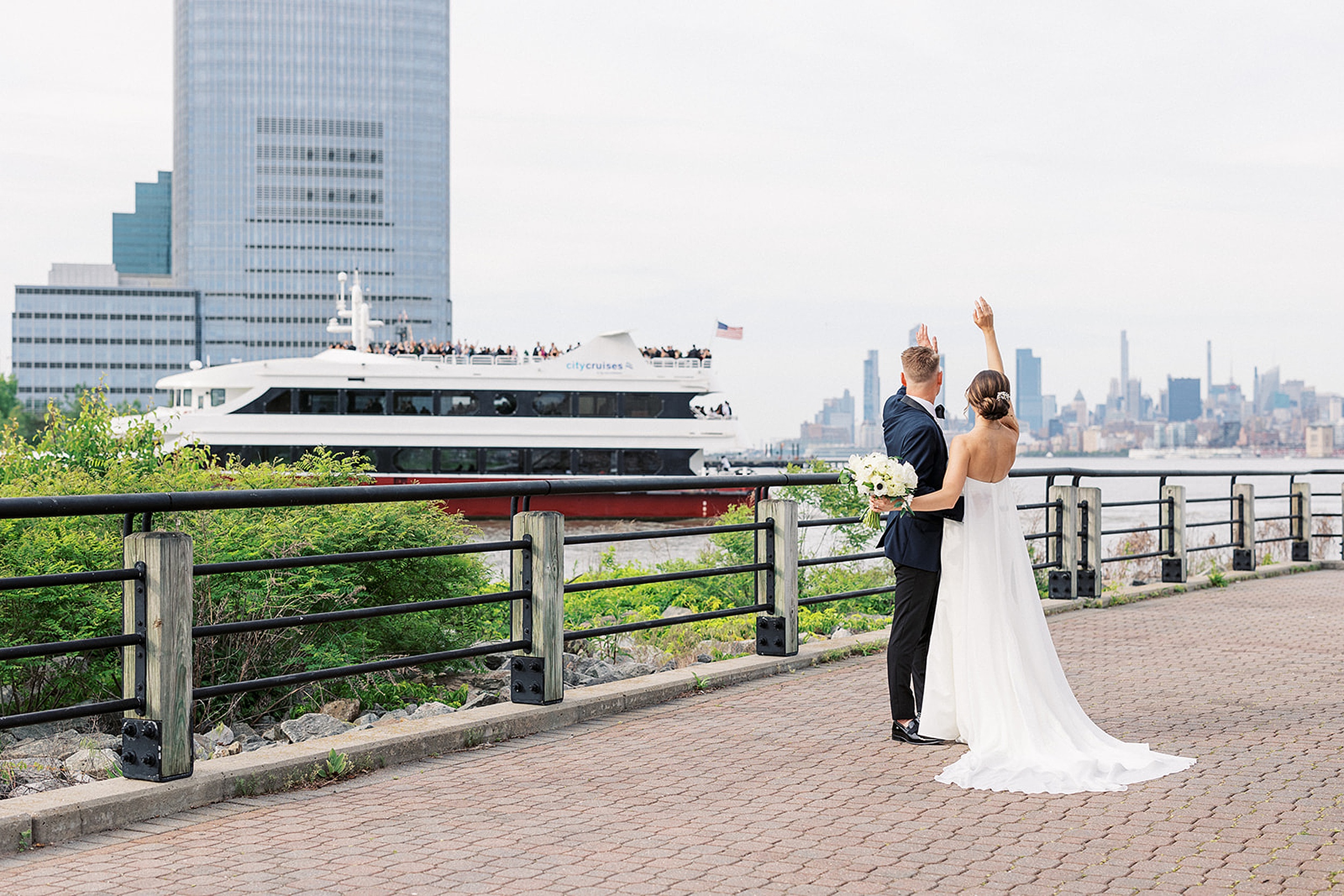 Newlyweds wave and to a city cruise boat that is cheering for them
