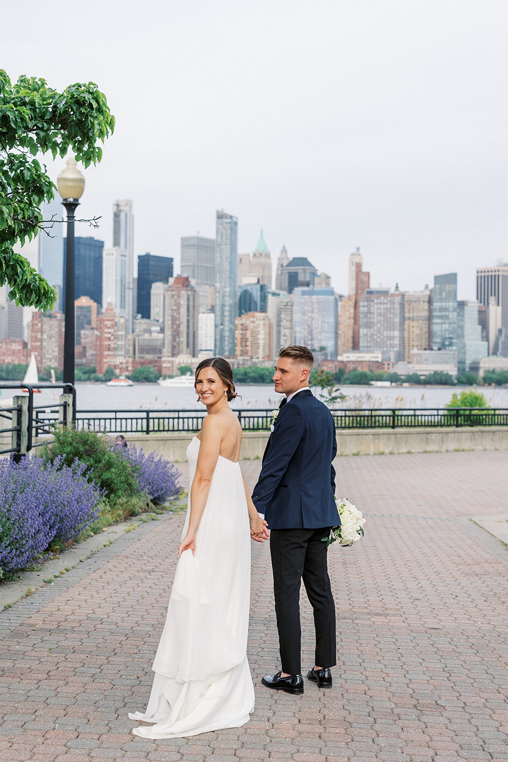 Newlyweds walk hand in hand through a park across the river from New York City