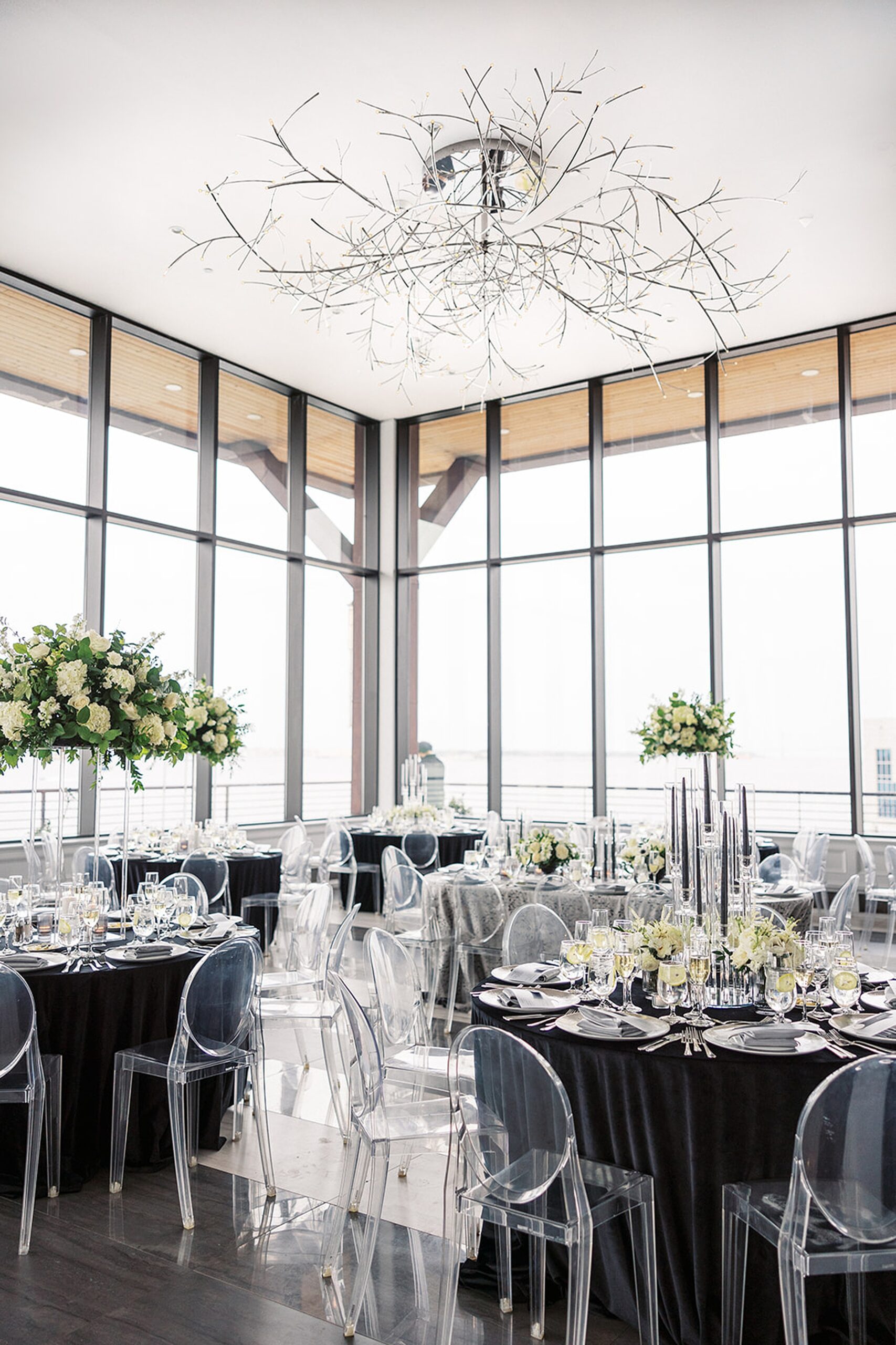 Details of a wedding reception venue with black linens and clear plastic chairs beneath a modern chandelier