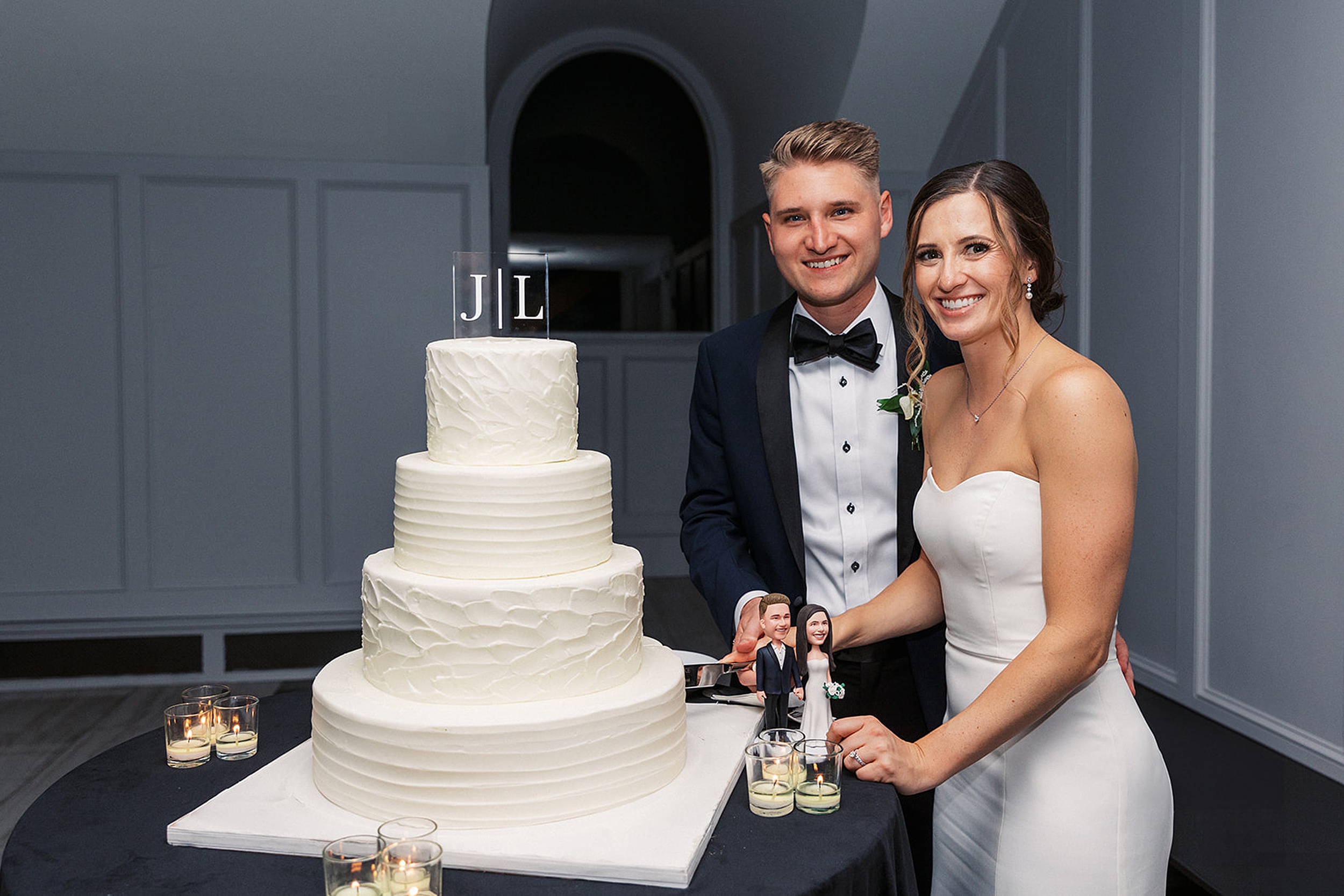 Newlyweds stand together as they cut their four tier white cake and hold the knife together