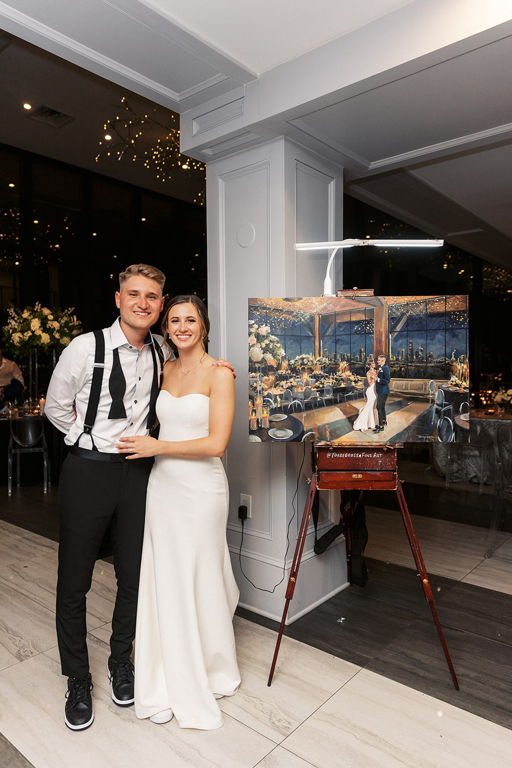 Newlyweds stand next to a painting of them dancing at their Hudson House wedding