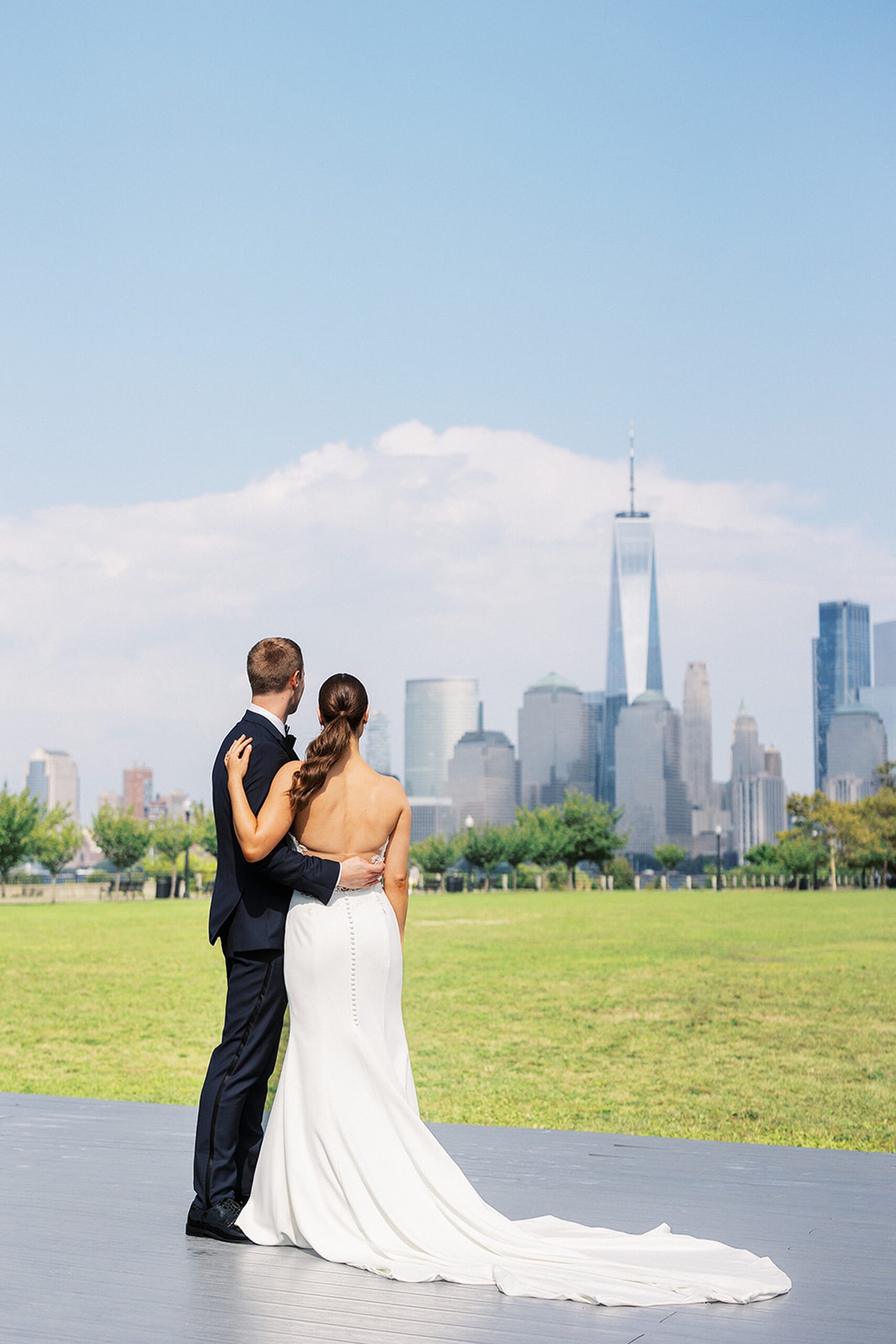 Newlyweds stare off at the Manhattan skyline from a riverfront boardwalk after their Liberty House Wedding