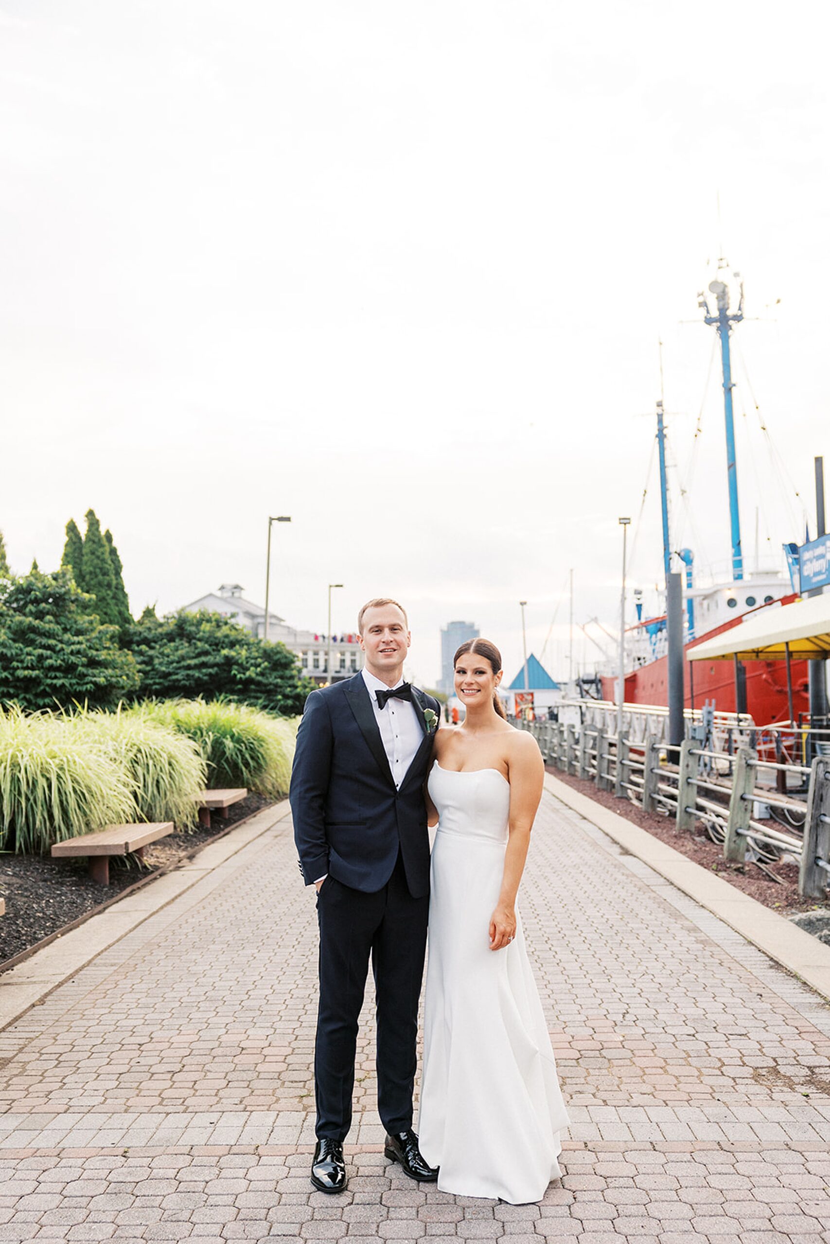 Newlyweds stand together on a riverfront park path by boats for their Liberty House Wedding