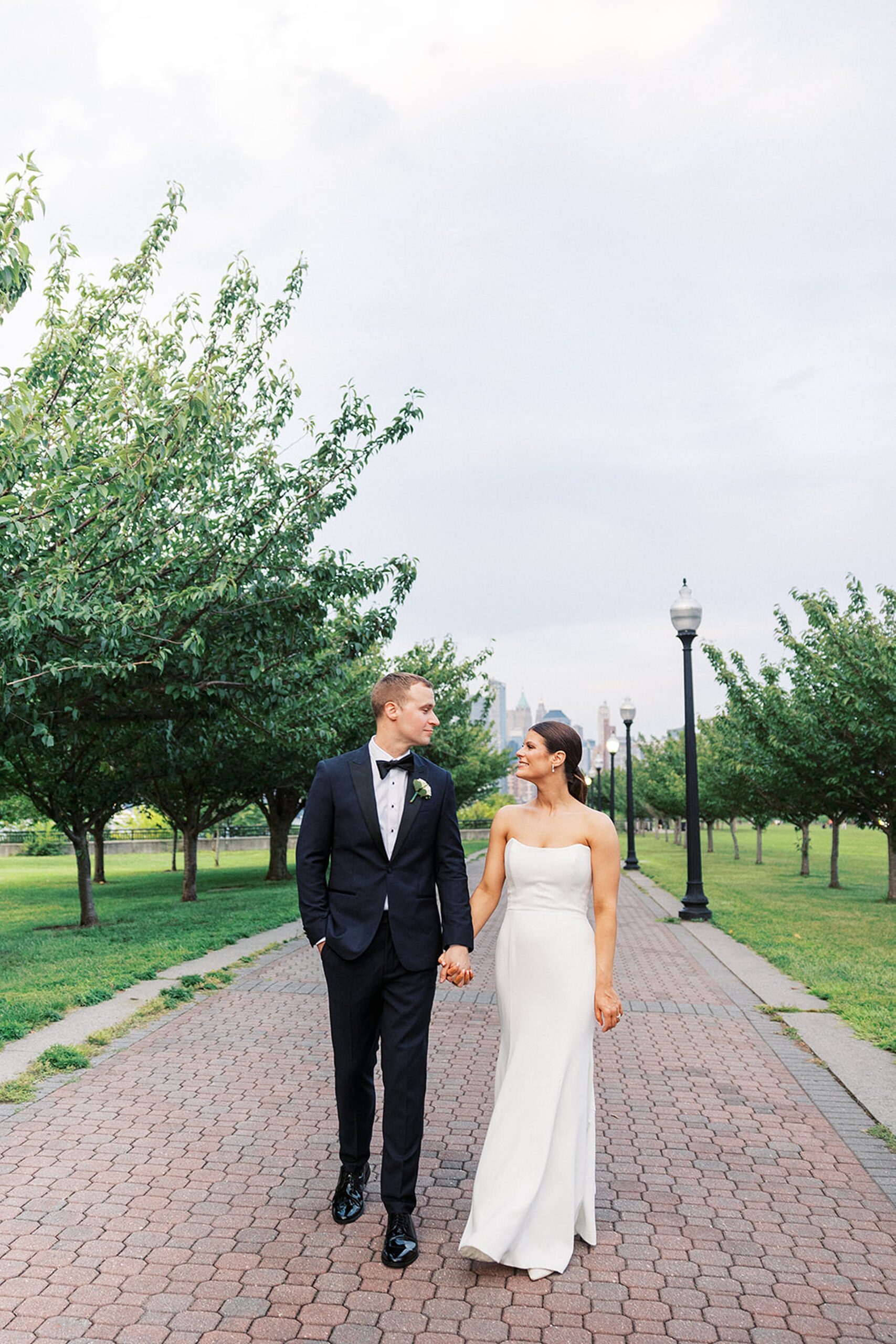 Newlyweds walk holding hands down a brick paved park path
