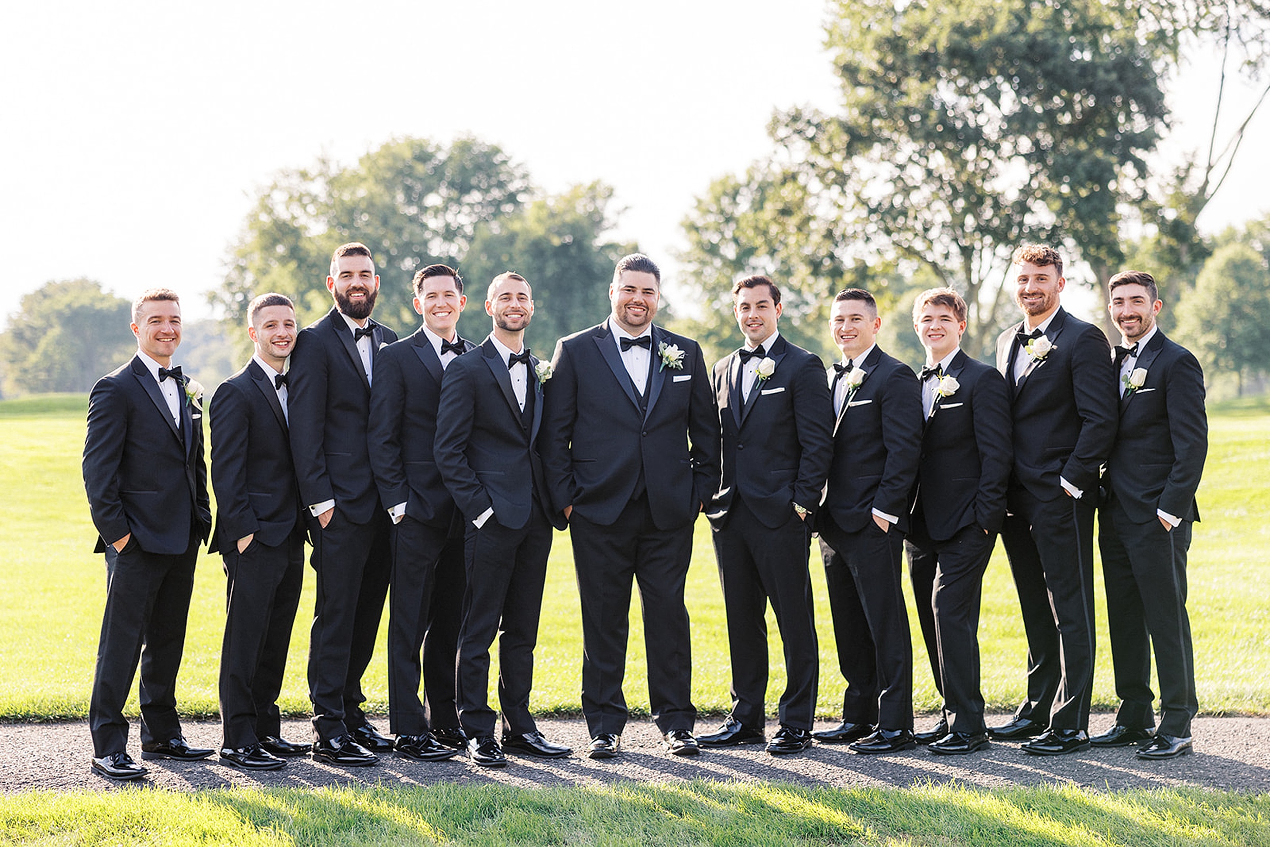 A groom stands in the middle of his ten groomsmen on a golf course path