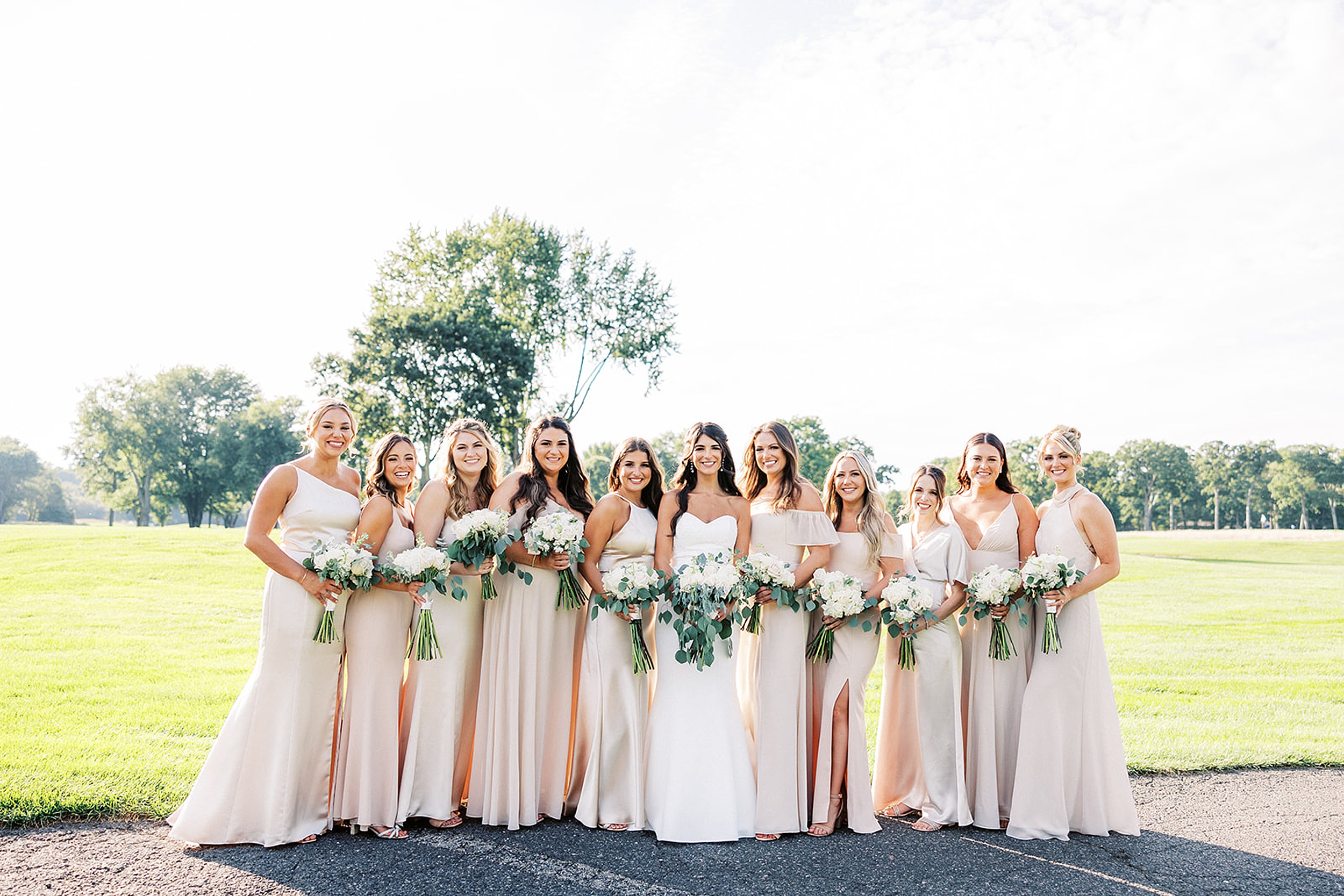 A bride stands amongst her large bridal party on the edge of a golf course at her edgewood country club wedding