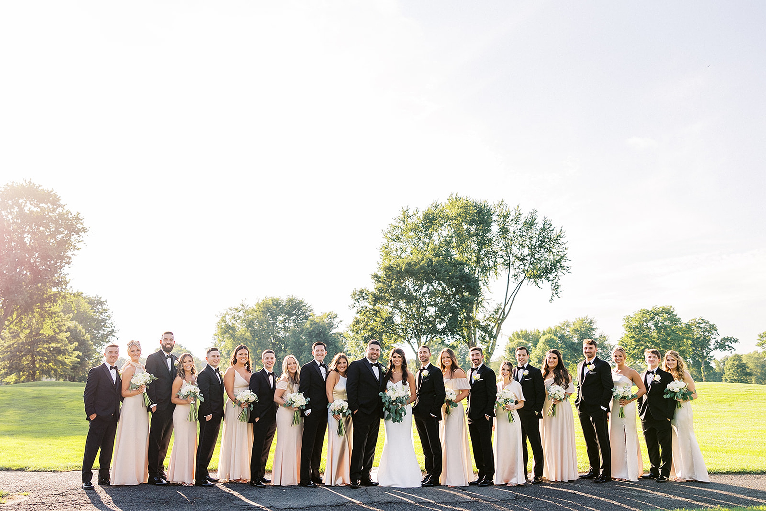 Newlyweds stand in line with their large wedding party at sunset on a golf course