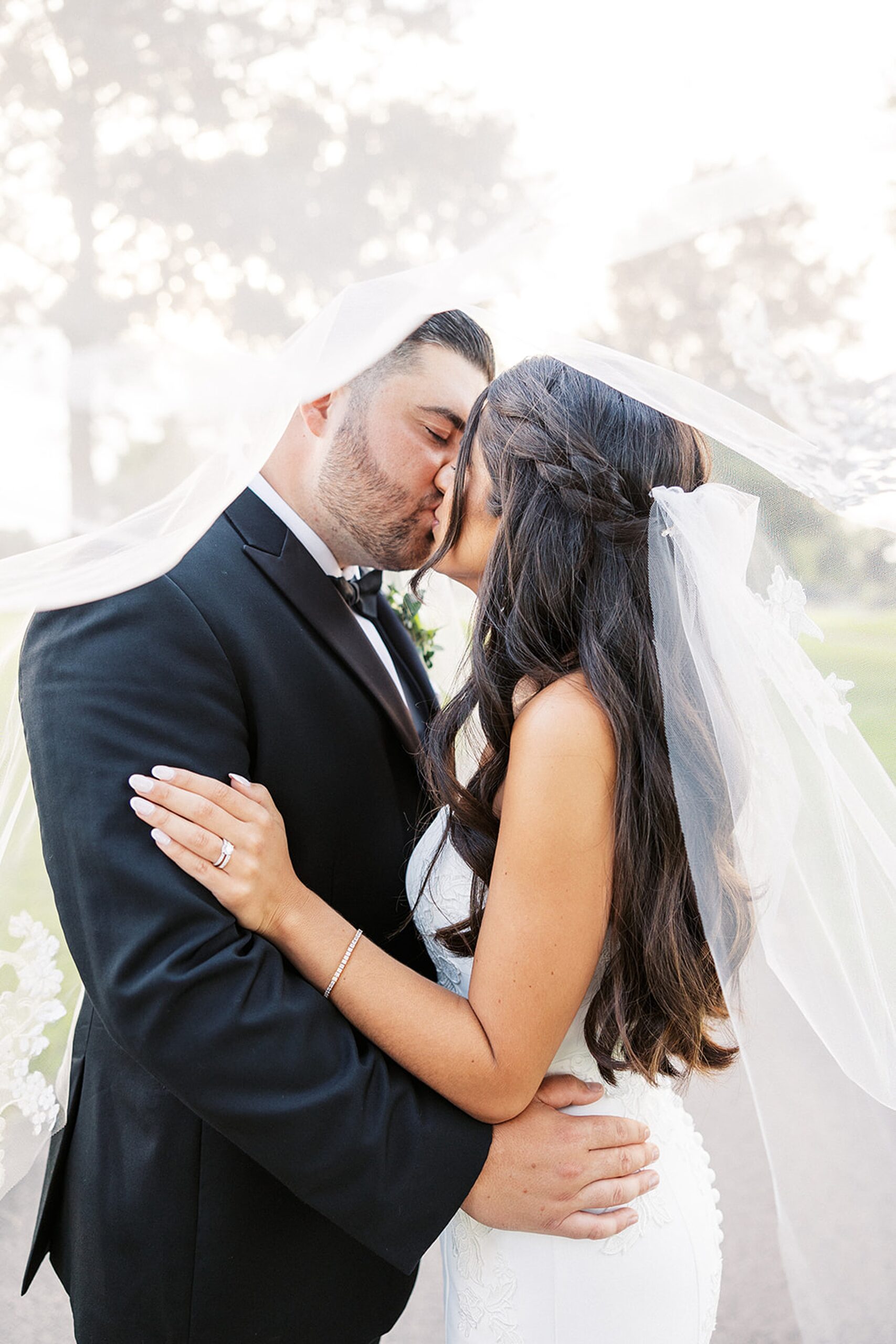 Newlyweds kiss while standing under the long veil
