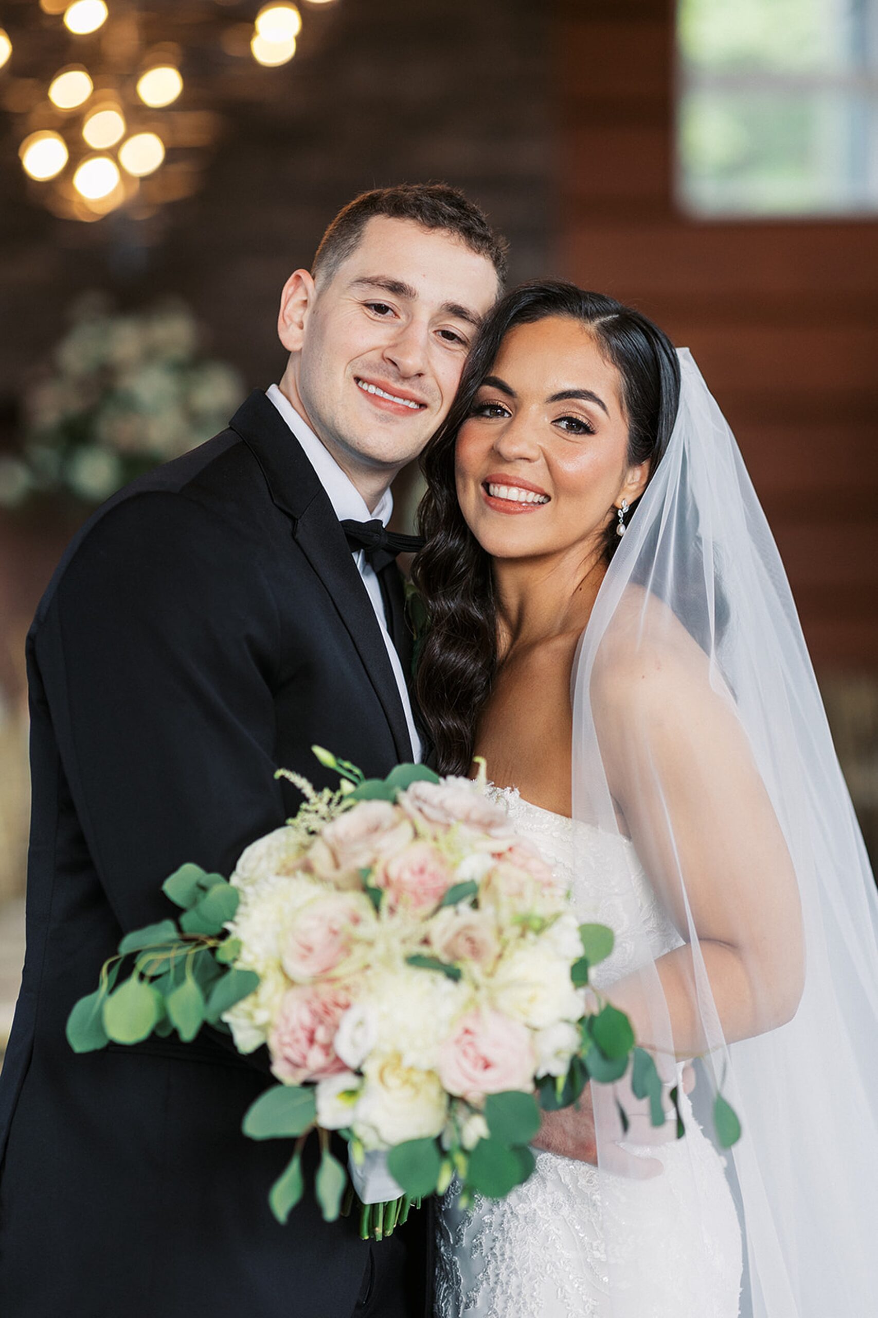Newlyweds embrace while standing in their reception venue holding the bouquet