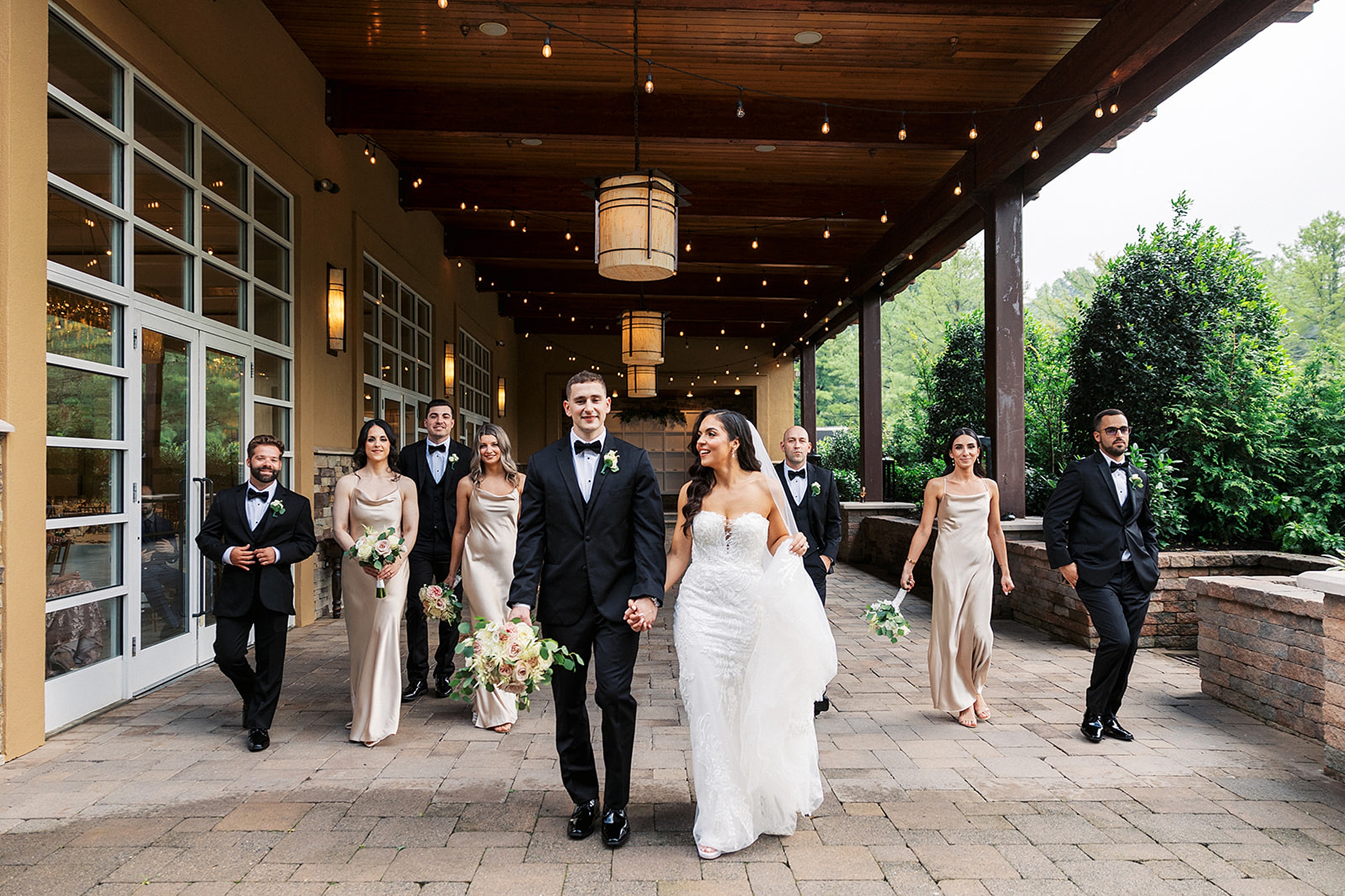 Newlyweds hold hands and walk through the patio of the Stonehouse At Stirling Ridge Wedding venue with their wedding party behind them