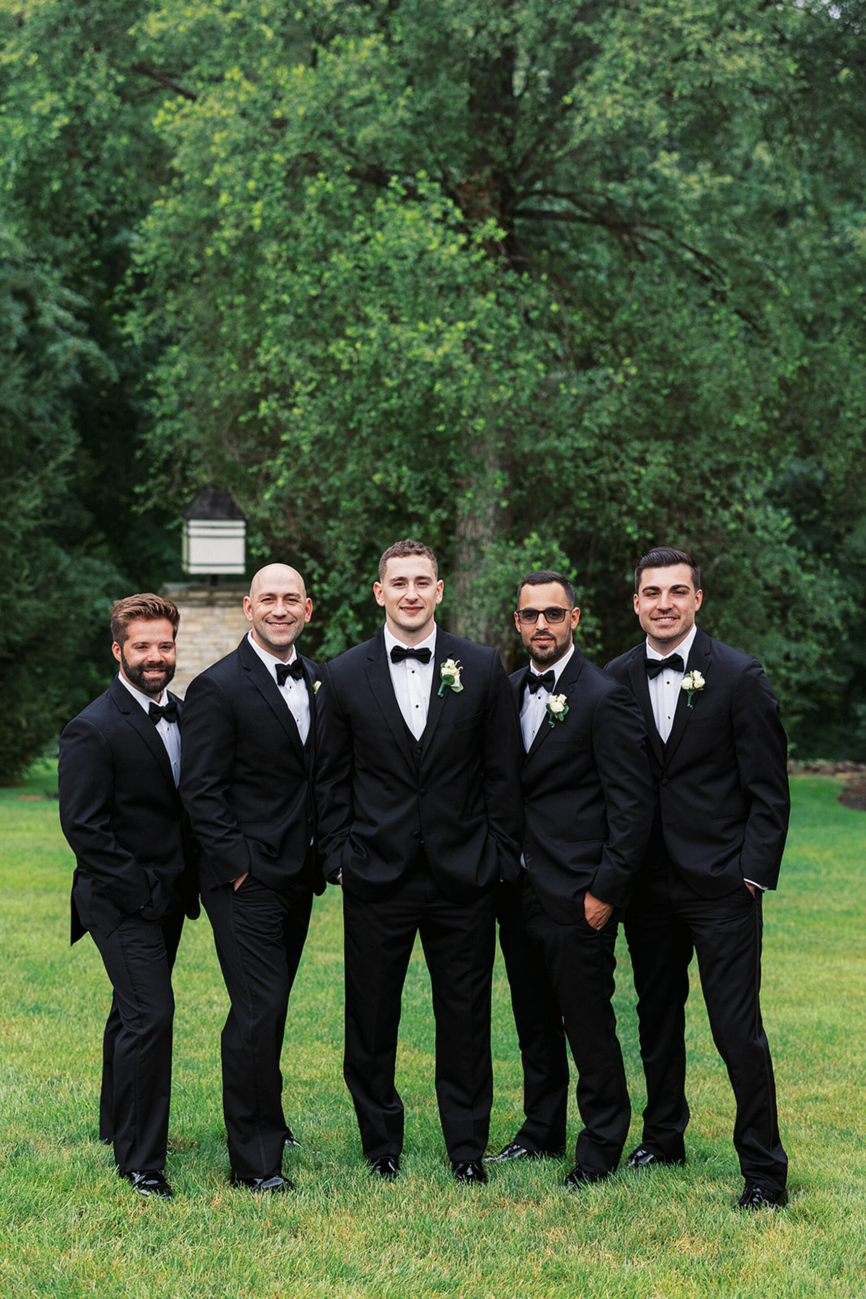A groom stands in a garden yard with his four groomsmen in black suits