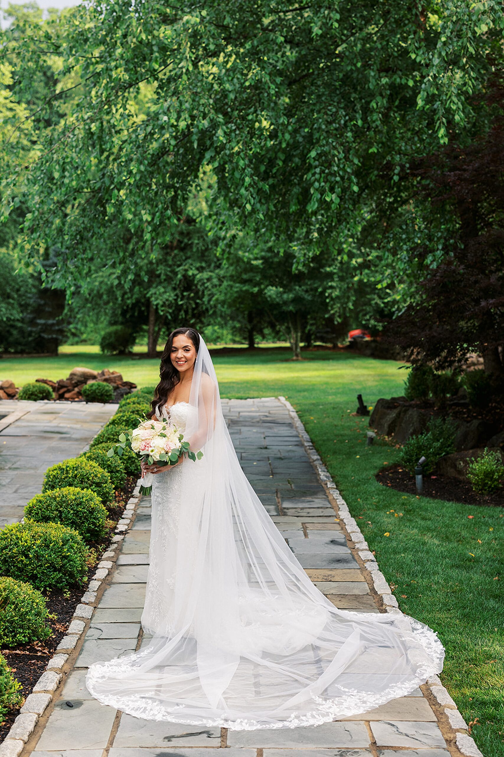 A bride stands in a stone garden path with her veil fully spread out