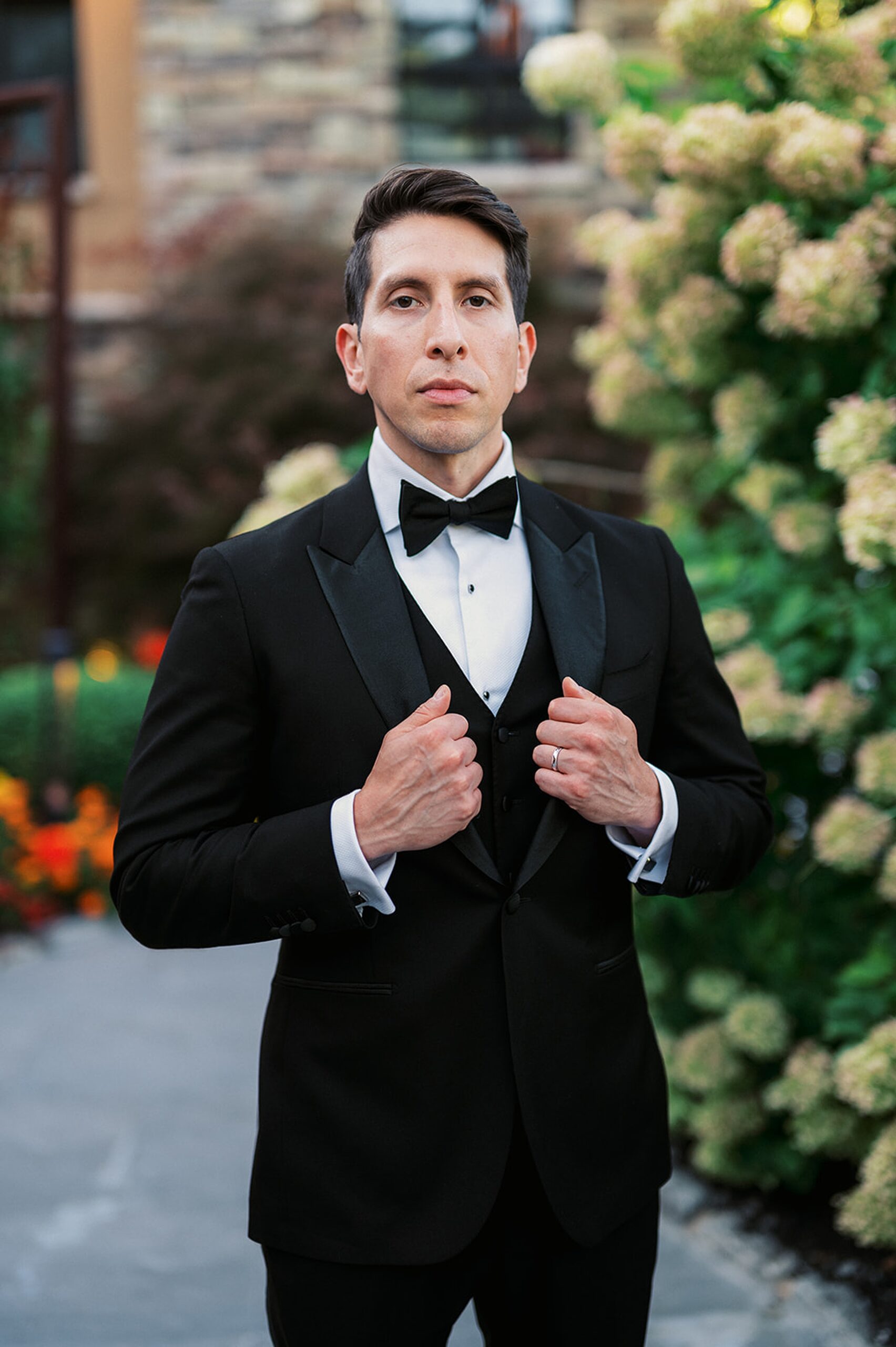 A groom holds his jacket lapels while standing in a garden before his Stonehouse At Stirling Ridge Wedding