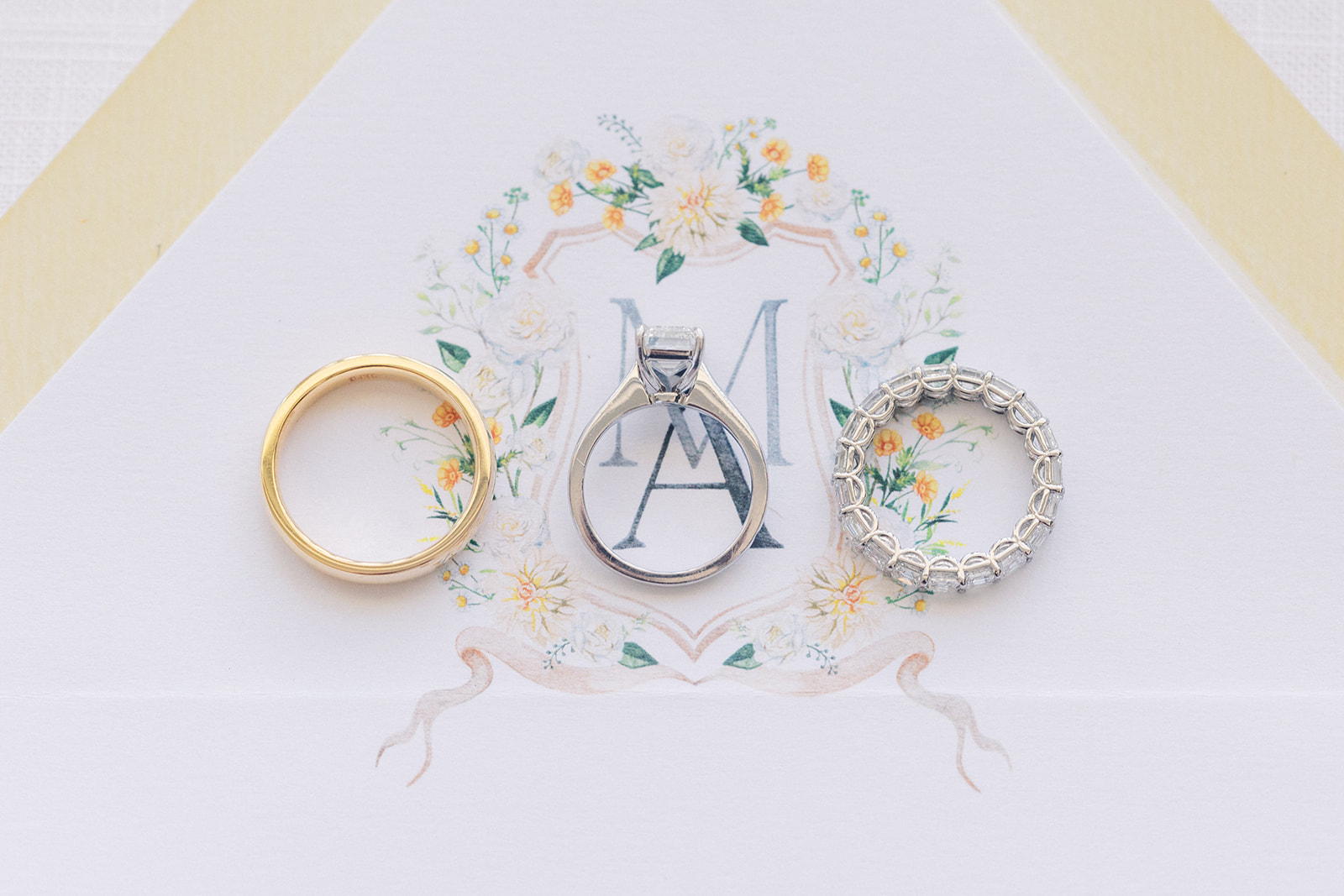 Wedding bands and an engagement ring sit together on an invitation