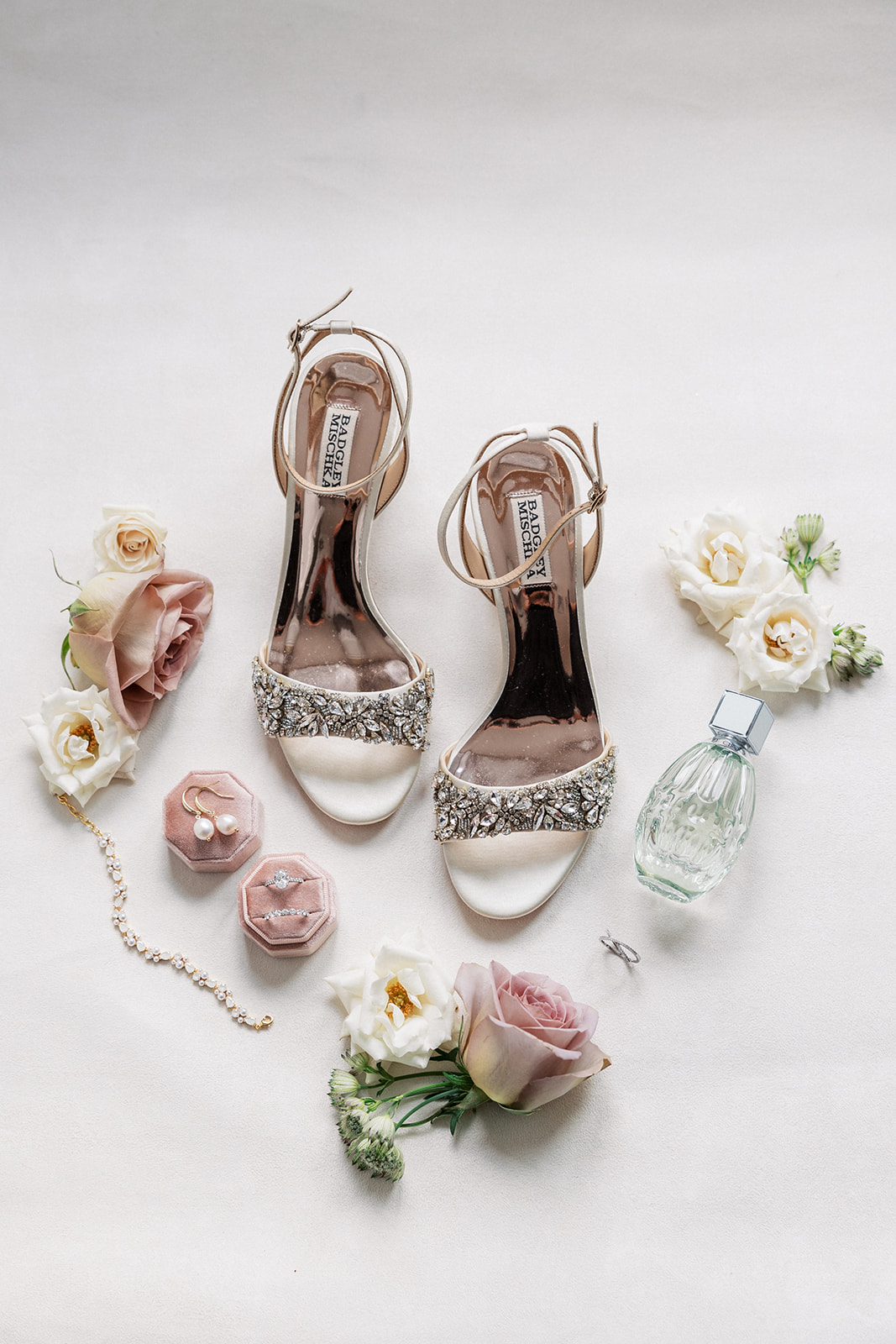 Bridal details sitting on a white table with shoes, perfume and jewelry