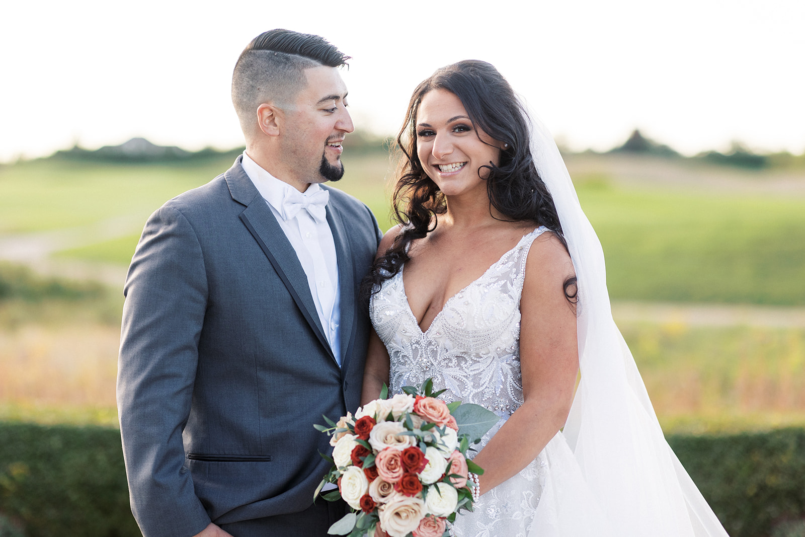 Newlyweds stand together holding the bouquet in a garden at sunset