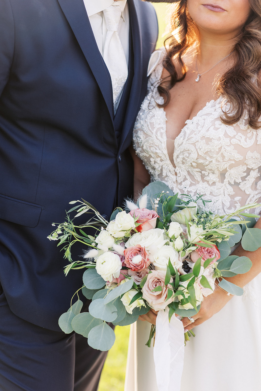 Details of a bride's white lace dress and her white and pink bouquet