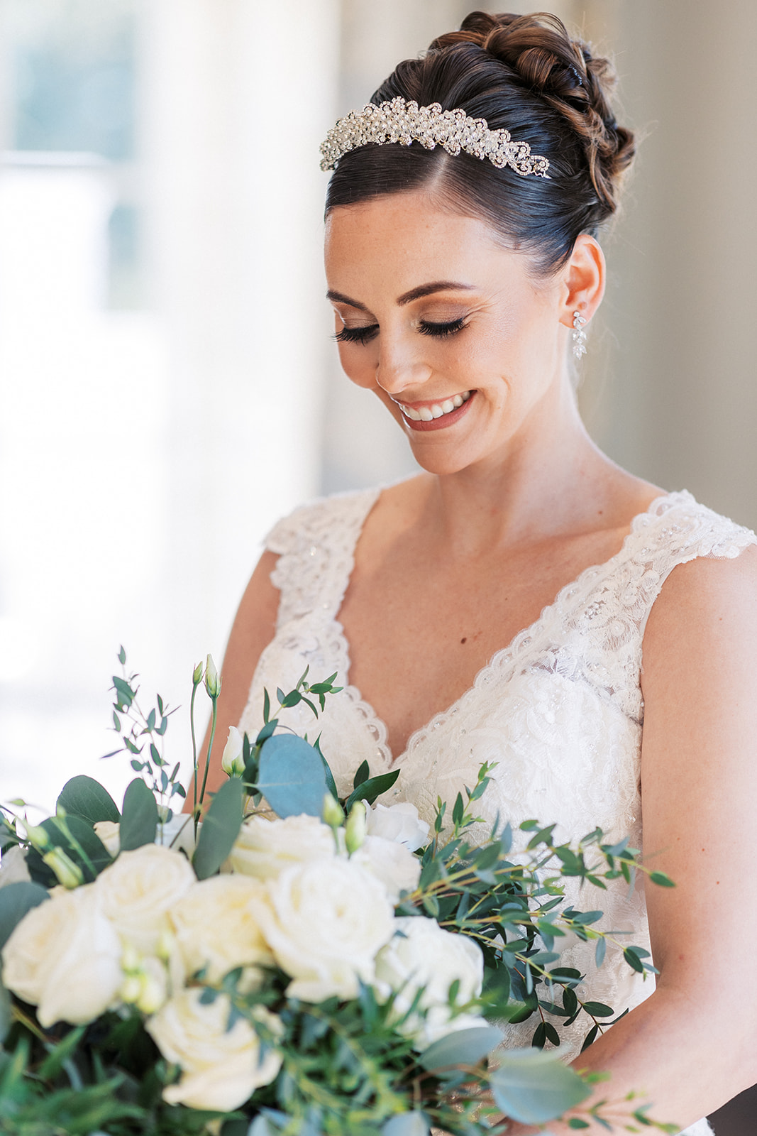A bride smiles down at her white rose bouquet while standing in a lace dress at a Hilton Short Hills Wedding