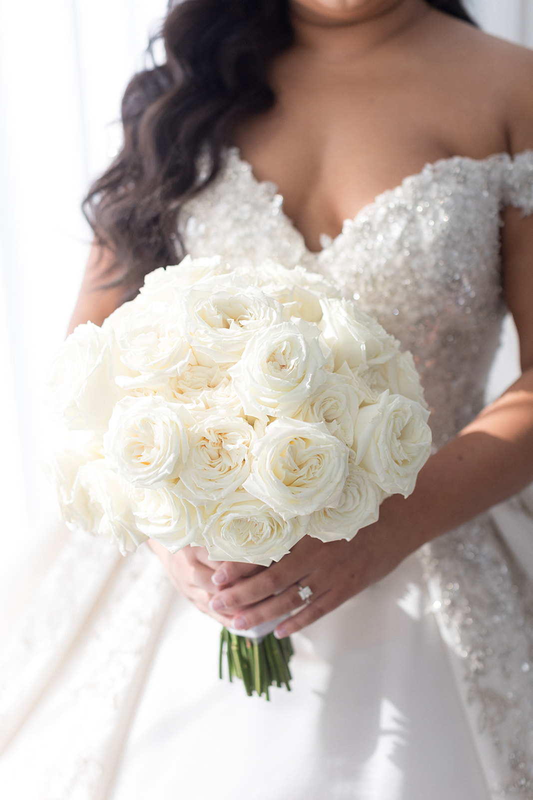 Details of a bride holding her white rose bouquet near a window