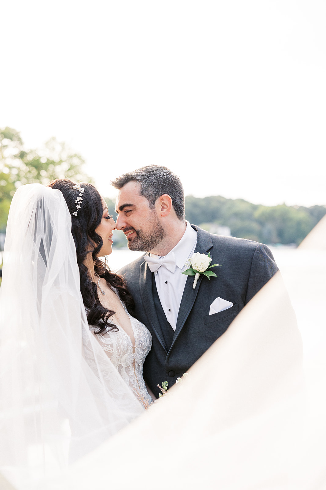 Newlyweds touch noses while standing by a lake