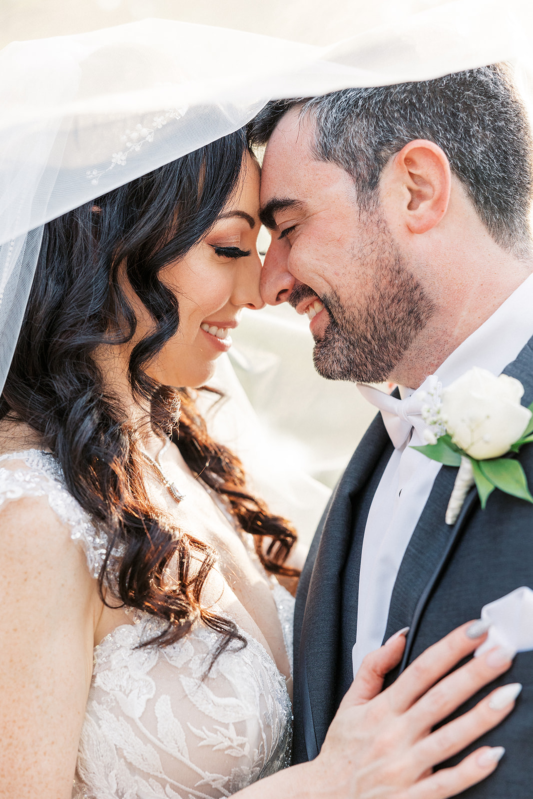 Newlyweds nuzzle noses while standing outside and hiding under the veil at a Lake Mohawk Country Club Wedding