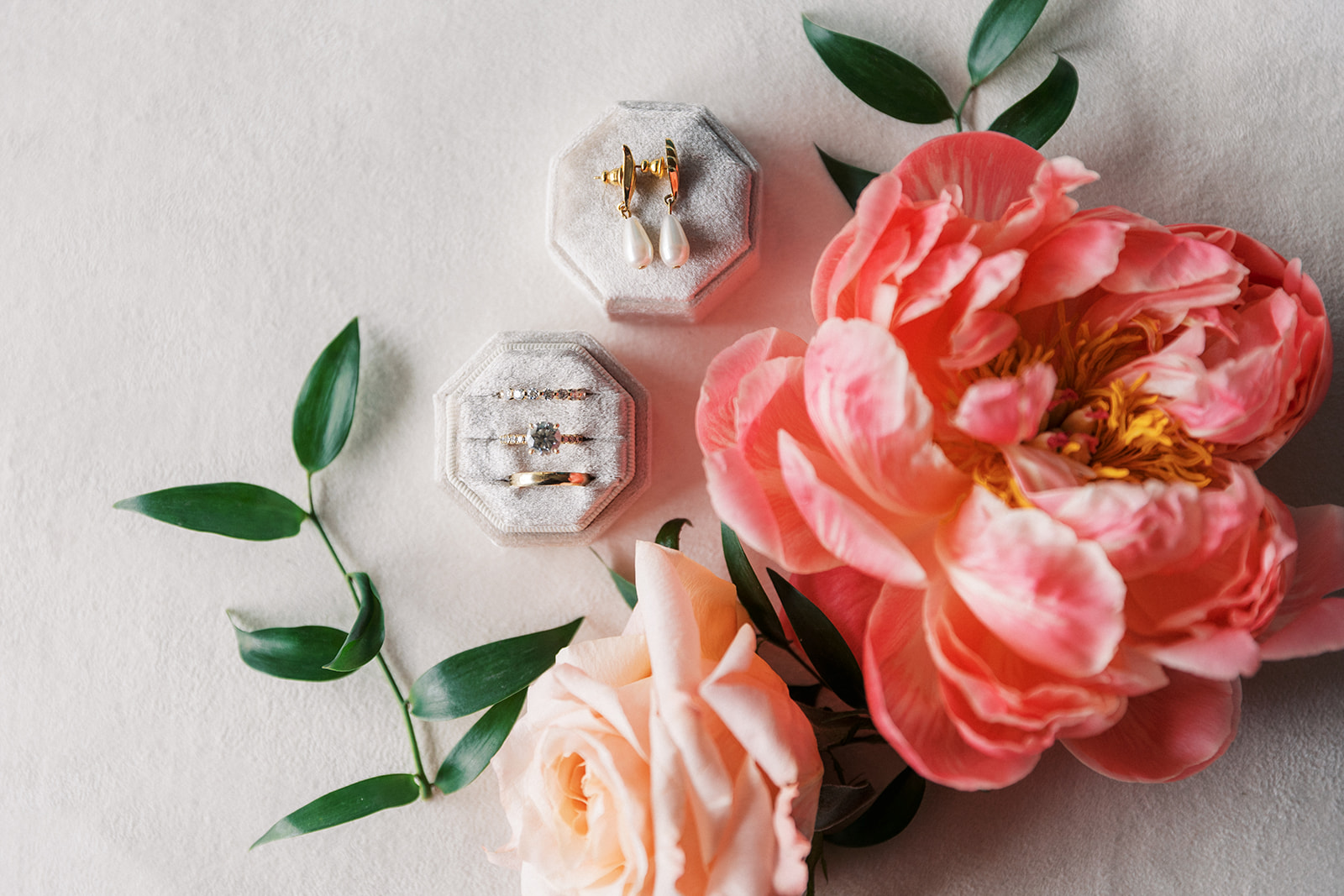 Details of wedding rings and pearl earrings with a pink flower