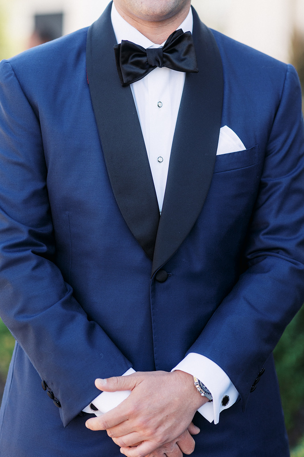 Details of a groom wearing a blue tuxedo jacket with a black bowtie