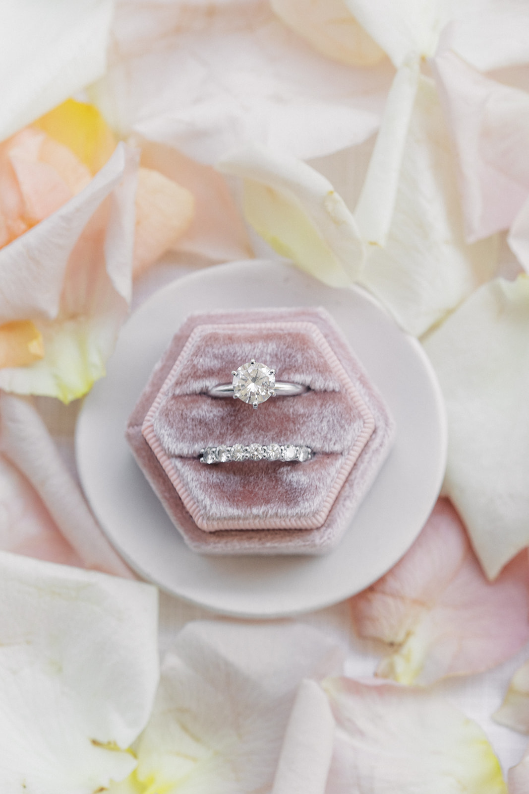 Details of a bride's wedding rings in a ring box surrounded by flower petals