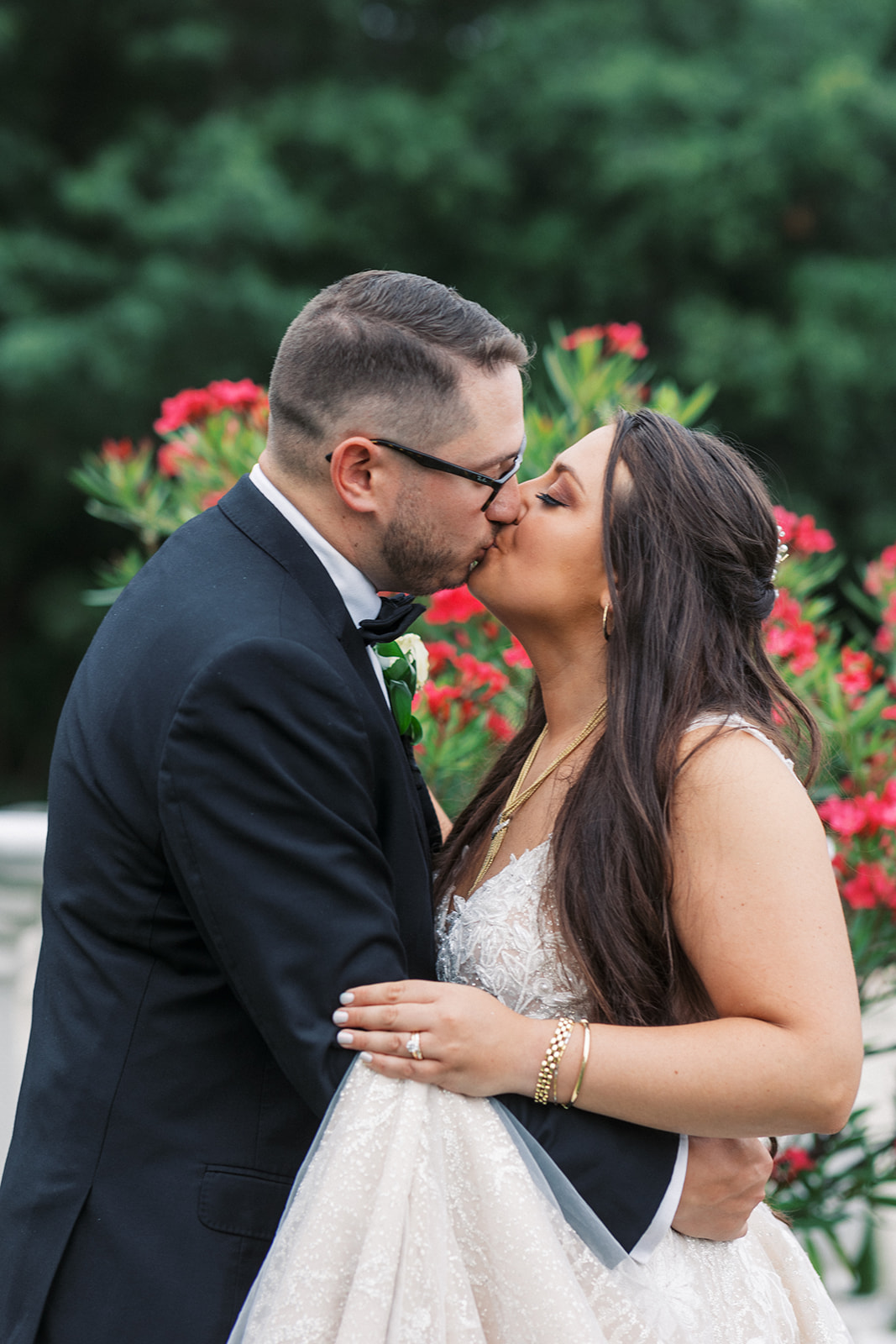 Newlyweds kiss while standing in a garden and holding the train of the white lace dress at The Manor NJ