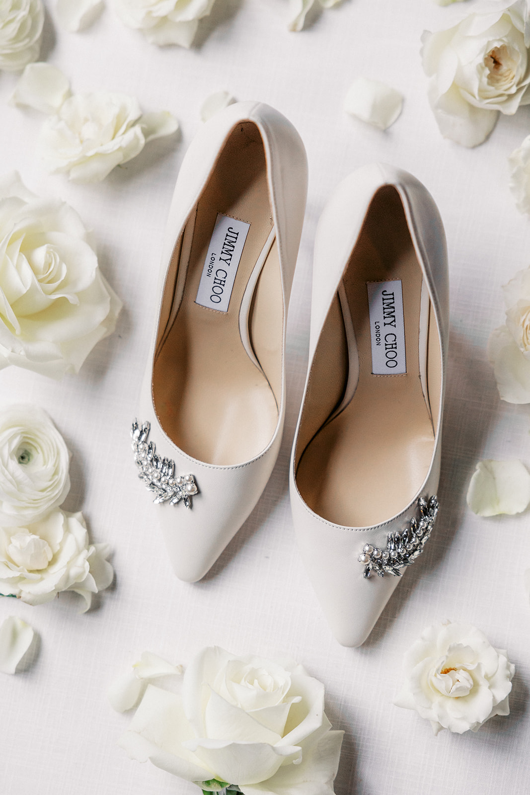Details of a brides white Jimmy Choo shoes surrounded by white roses