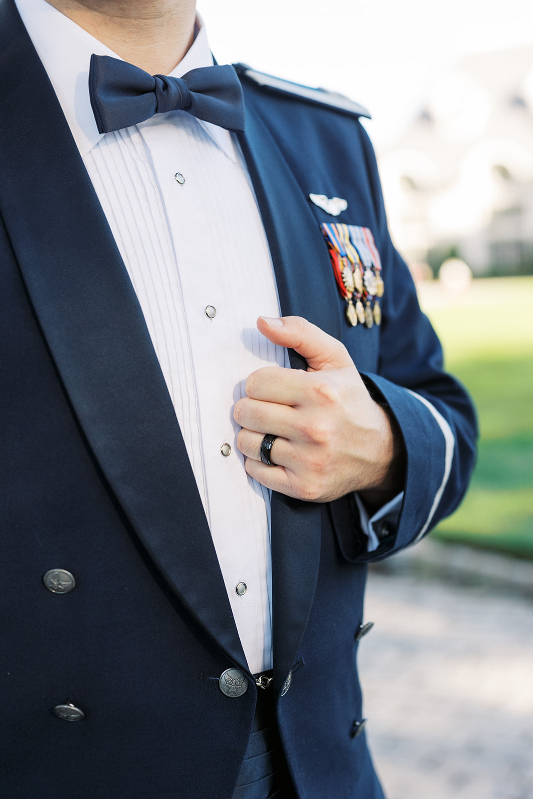 Details of a groom's decorated pilot's jacket as he holds the lapel with his ring hand at The Tides Estate Wedding venue