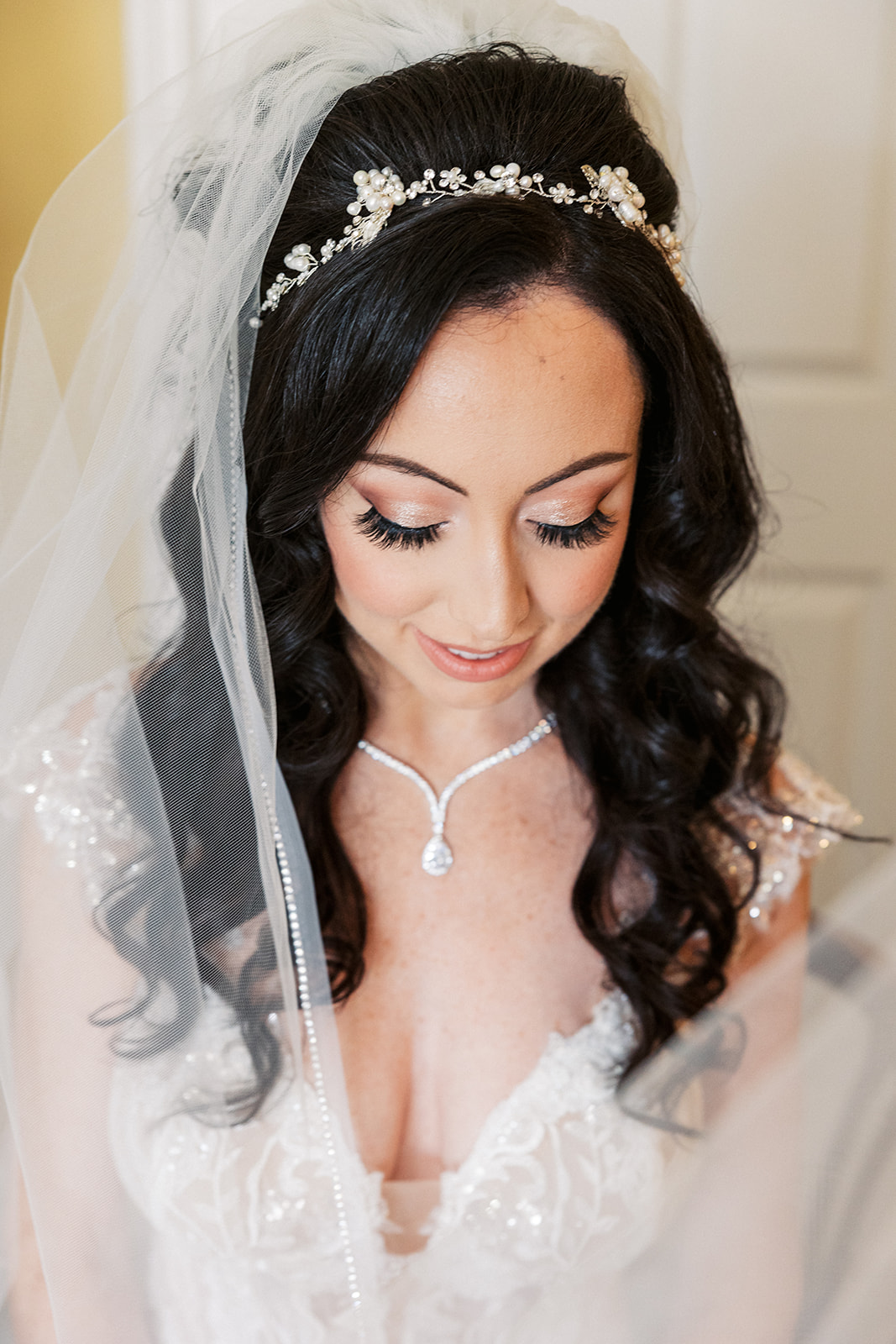 A bride gazes down at her lace dress while surrounded by her veil