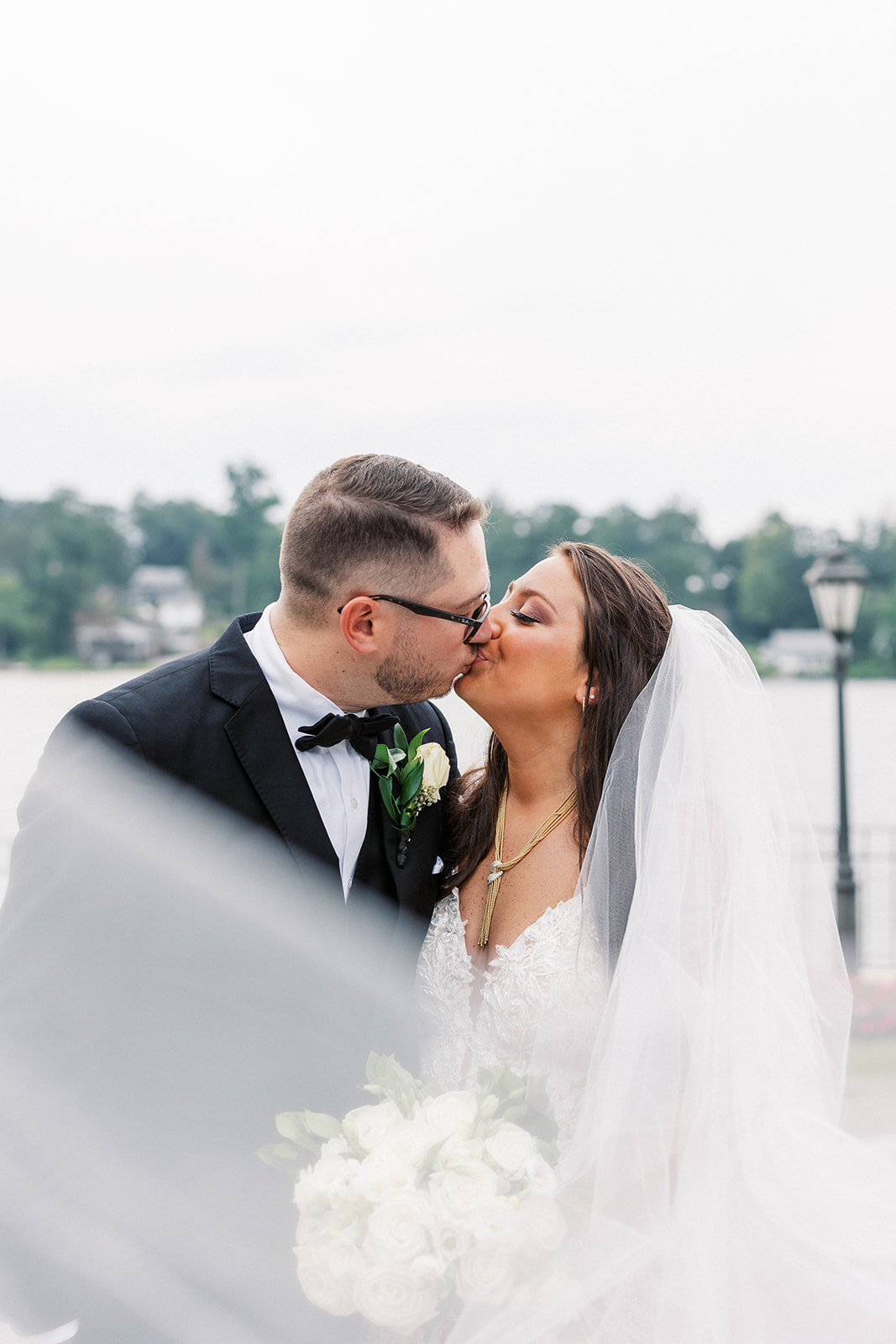 Newlyweds kiss while standing in a park wrapped in a long veil at a Waterside Events Wedding