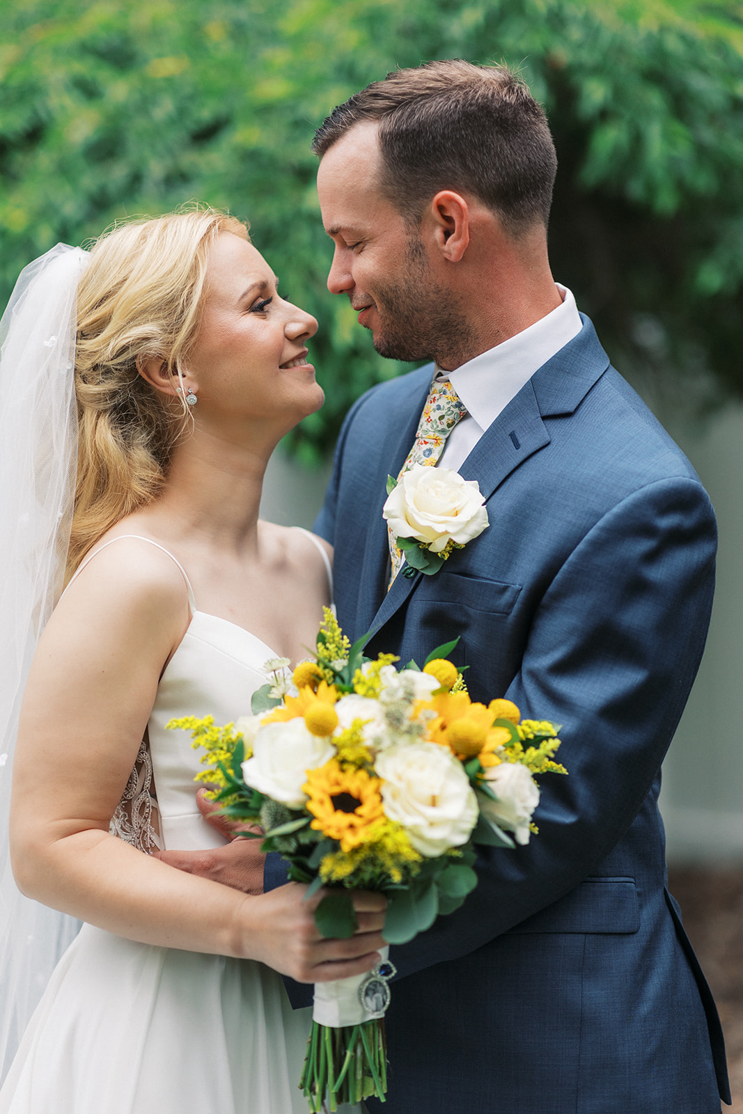 Newlyweds embrace and gaze into each other's eyes while the groom wears a blue suit and the bride holds her yellow and white bouquet at a Westmount Country Club Wedding
