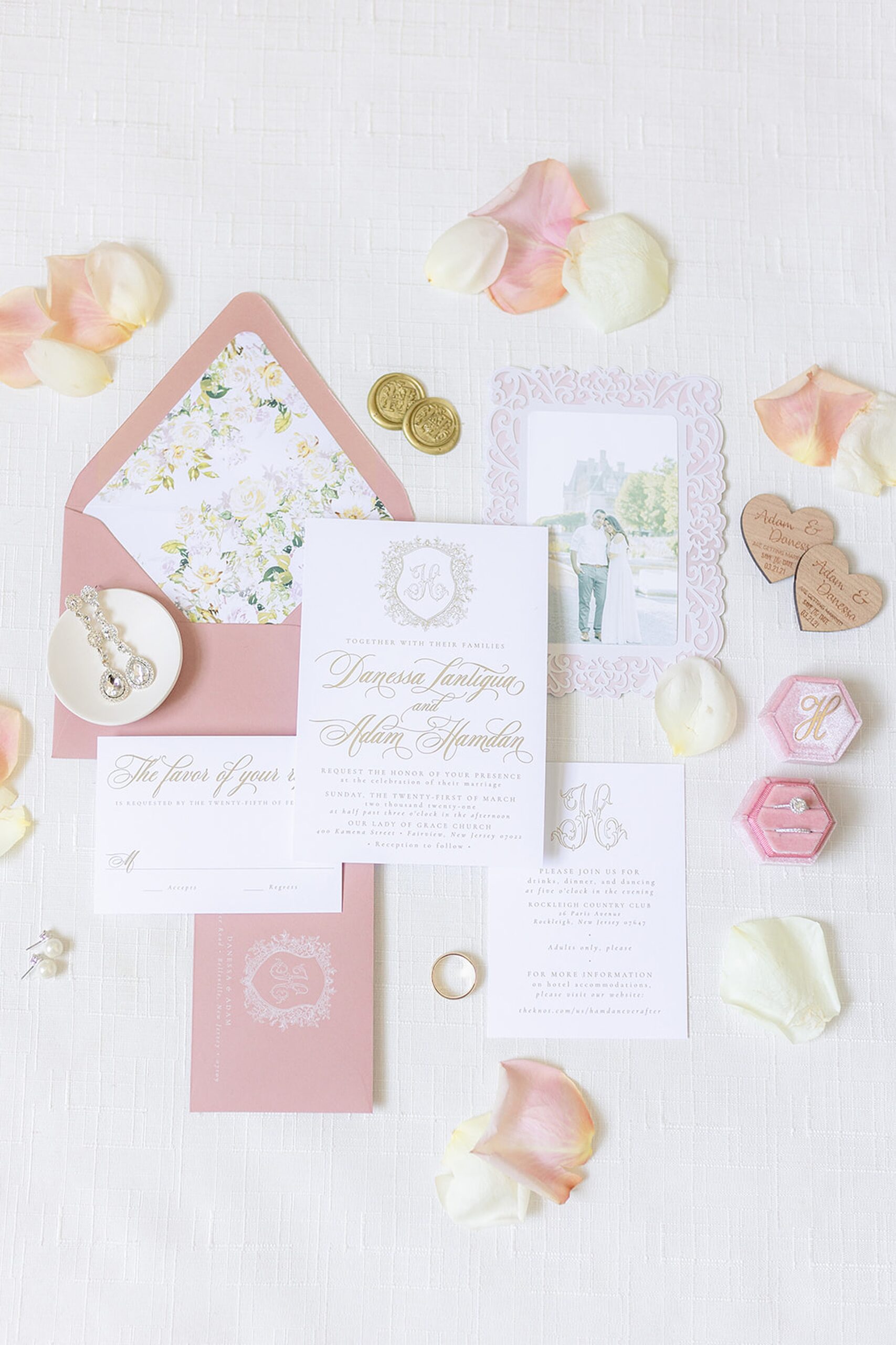 Details of wedding invitations and jewelry sitting on a white bed