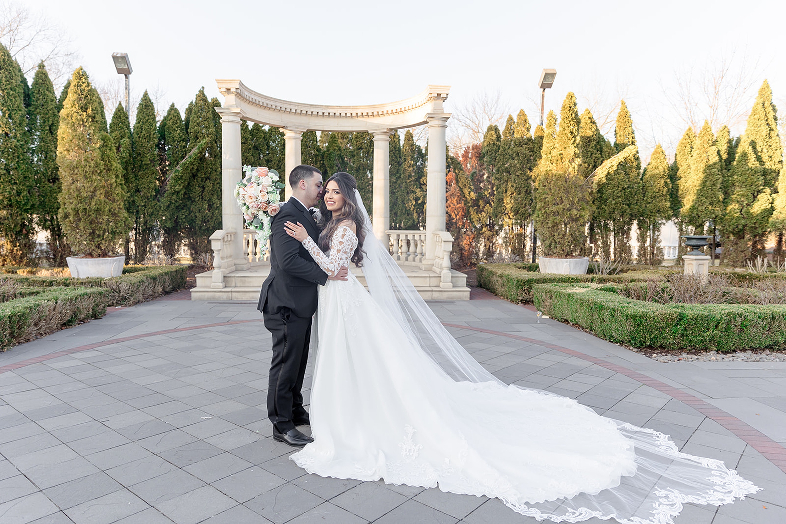 NEwlyweds embrace while standing in a stone garden patio